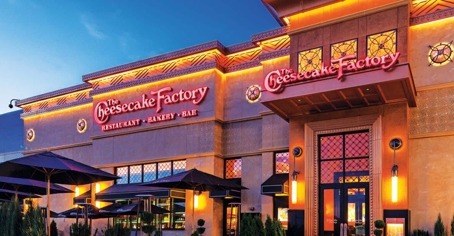 A Cheesecake Factory storefront lit up in the evening.