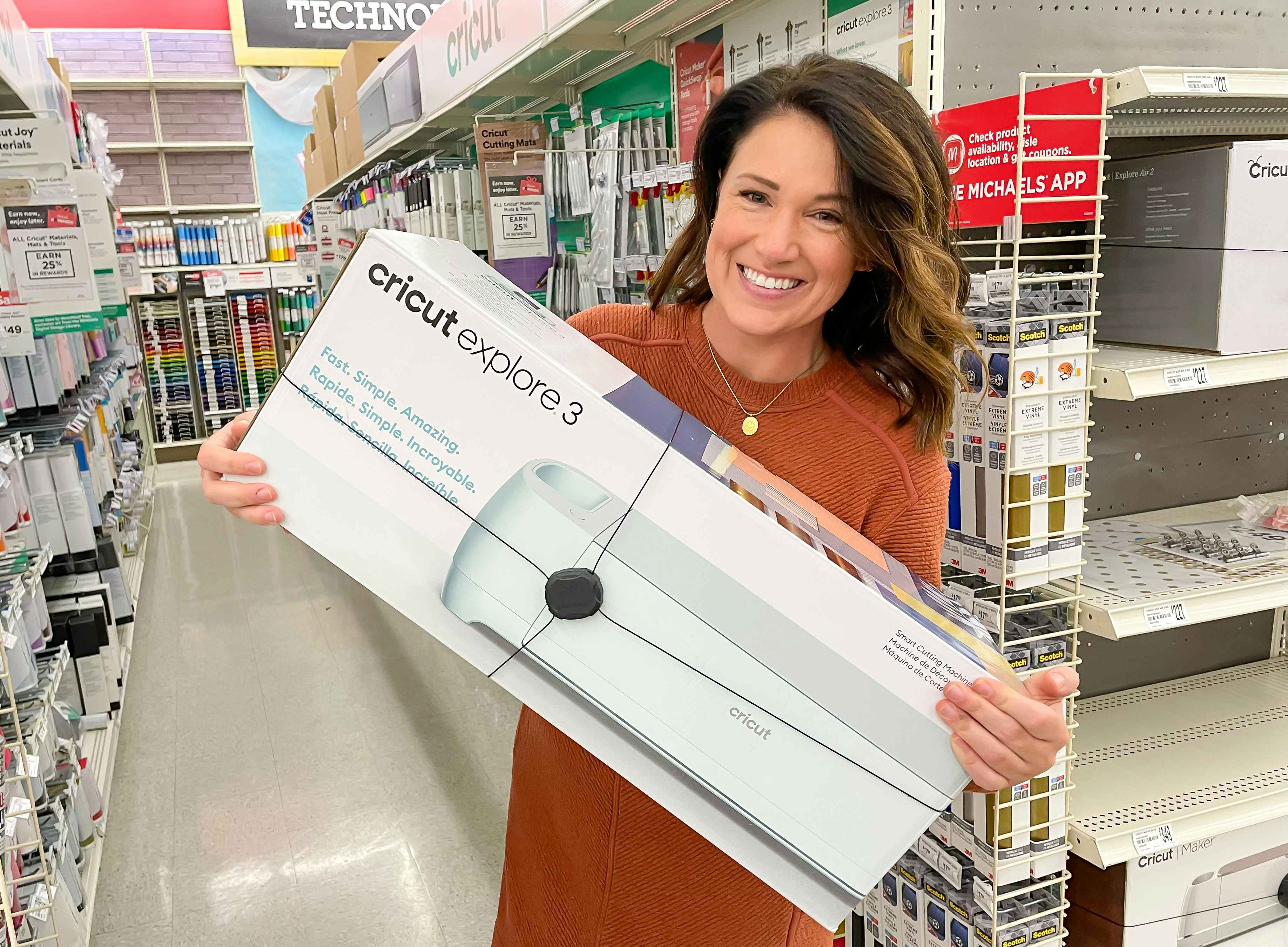 A person holding a Cricut Explore 3 machine in its box while standing in an aisle at Michaels
