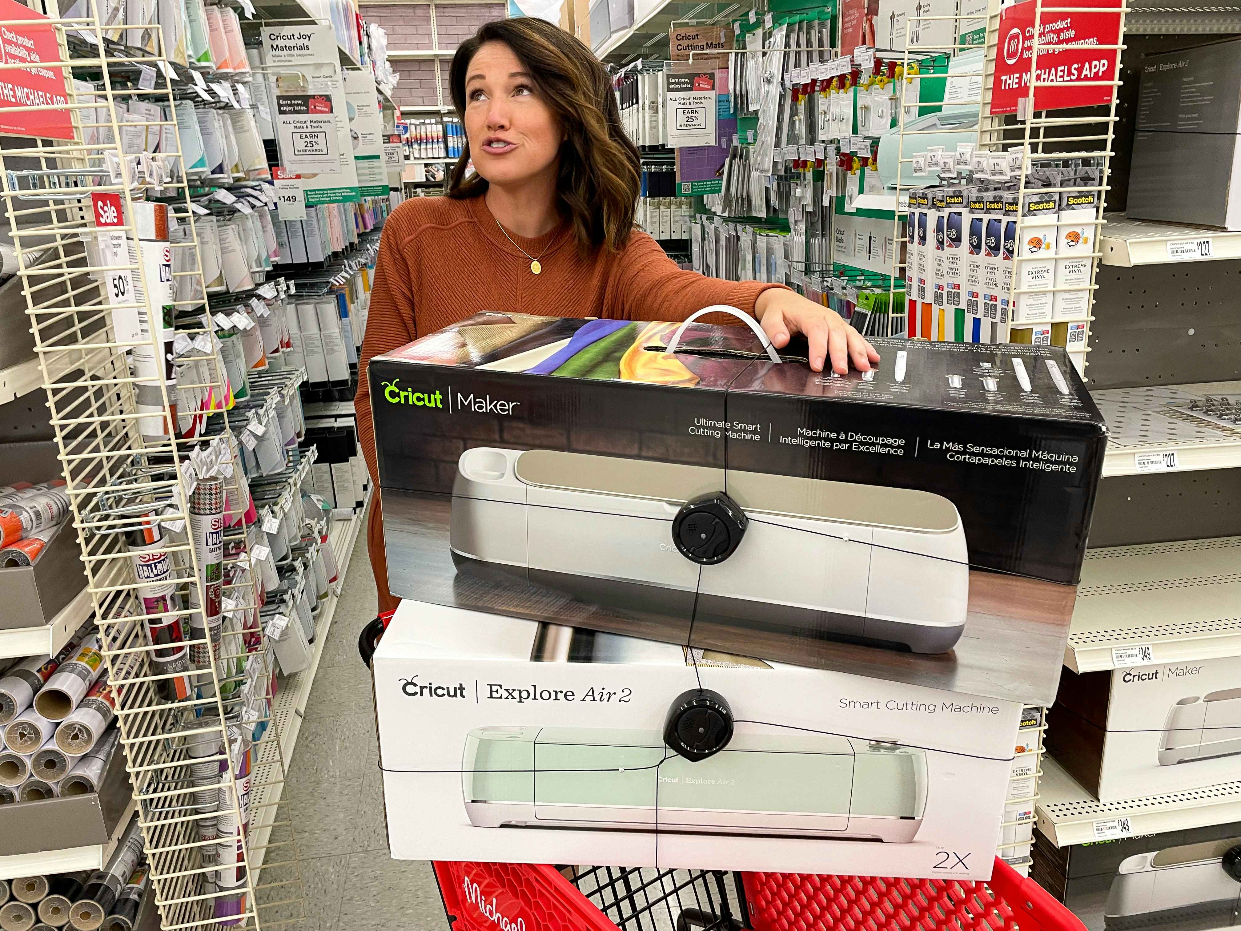 A person holding two Cricut machines stacked on top of a Michaels shopping cart inside Michaels.