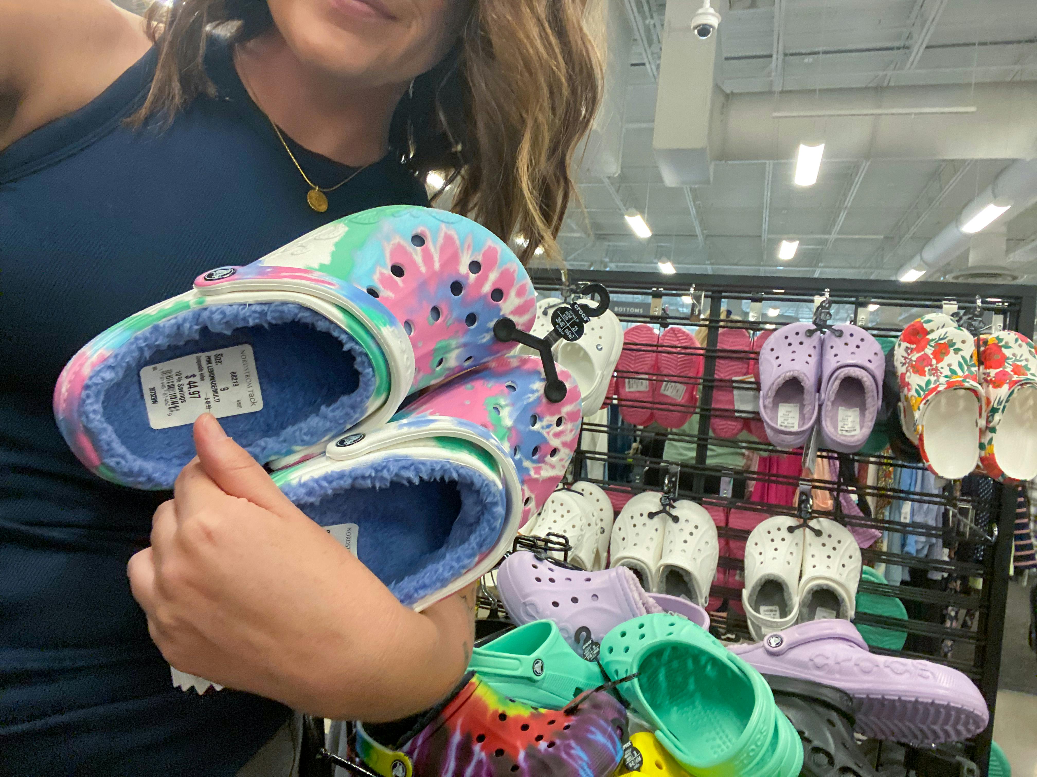 A woman holding a pair of Crocs in front of a Croc display at a shoe store.