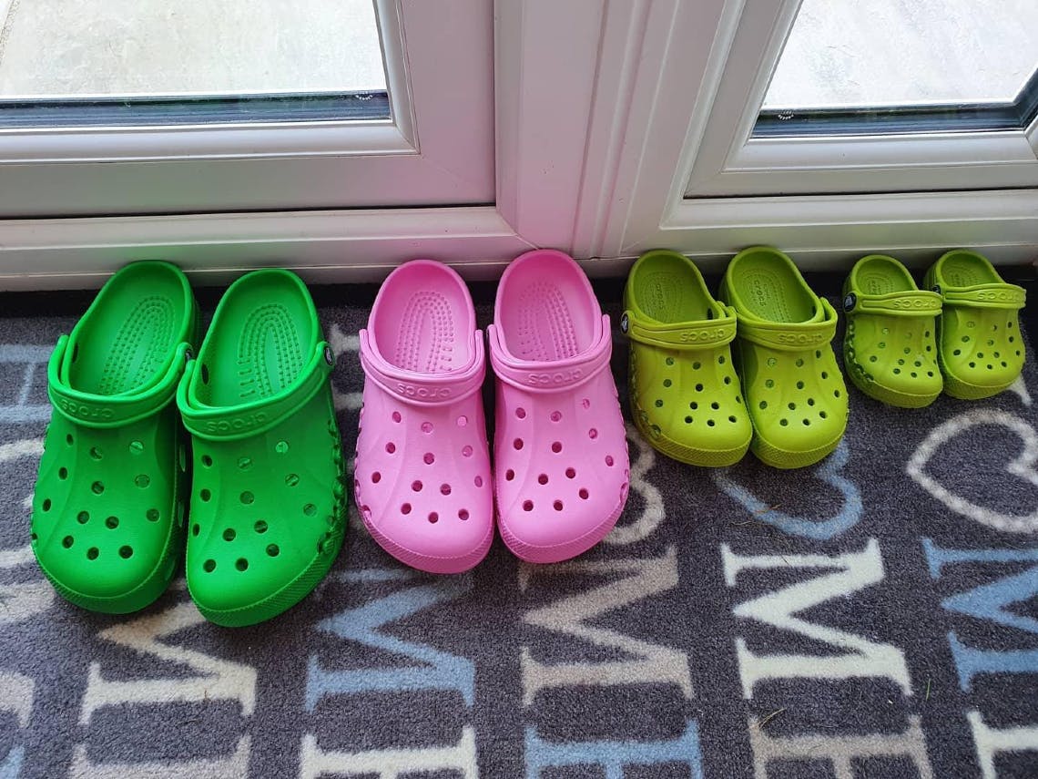 A family's four pairs of Crocs classic clogs lined up against the door on a doormat.