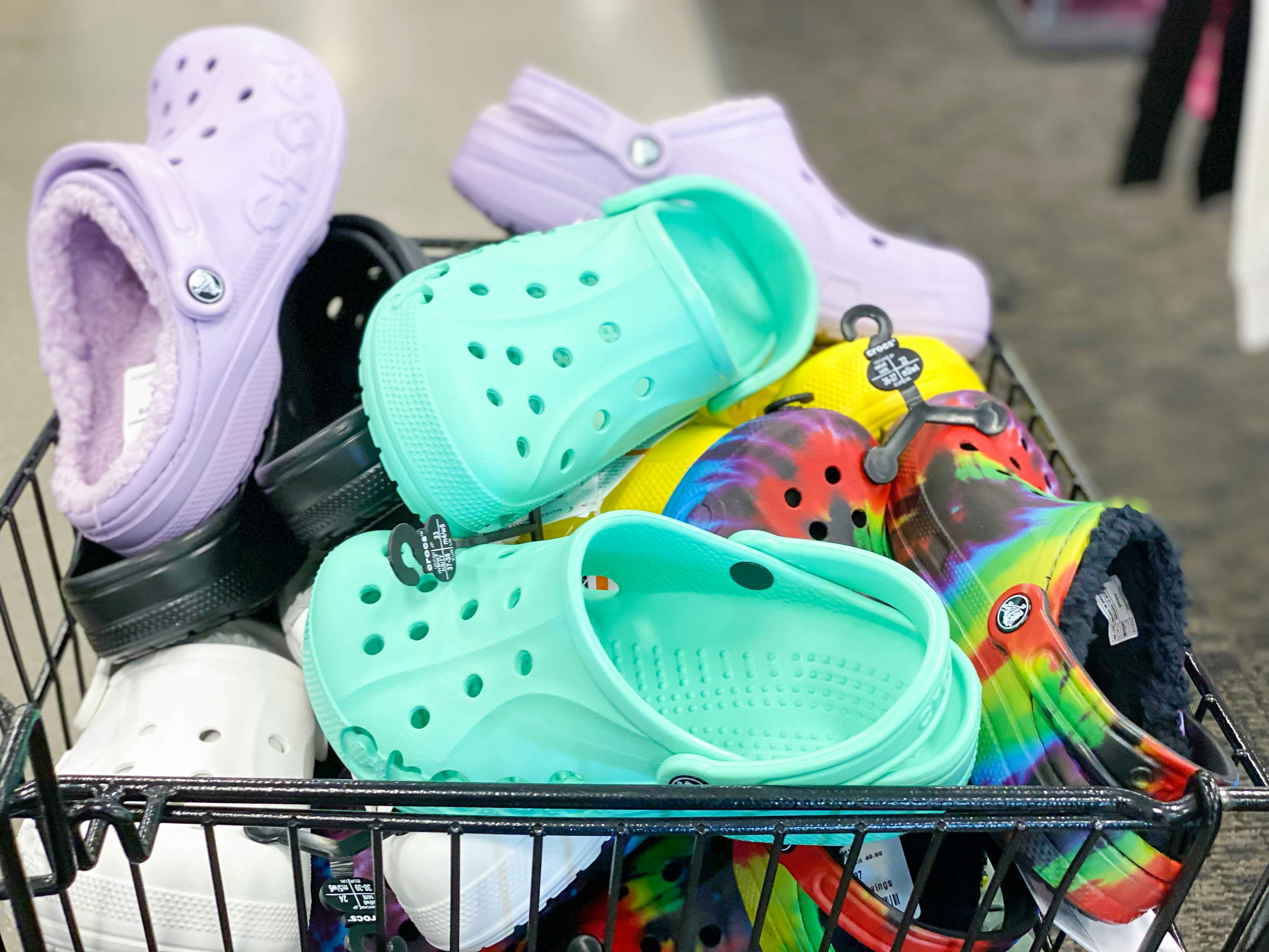 A shopping cart filled with pairs of Crocs inside a store.