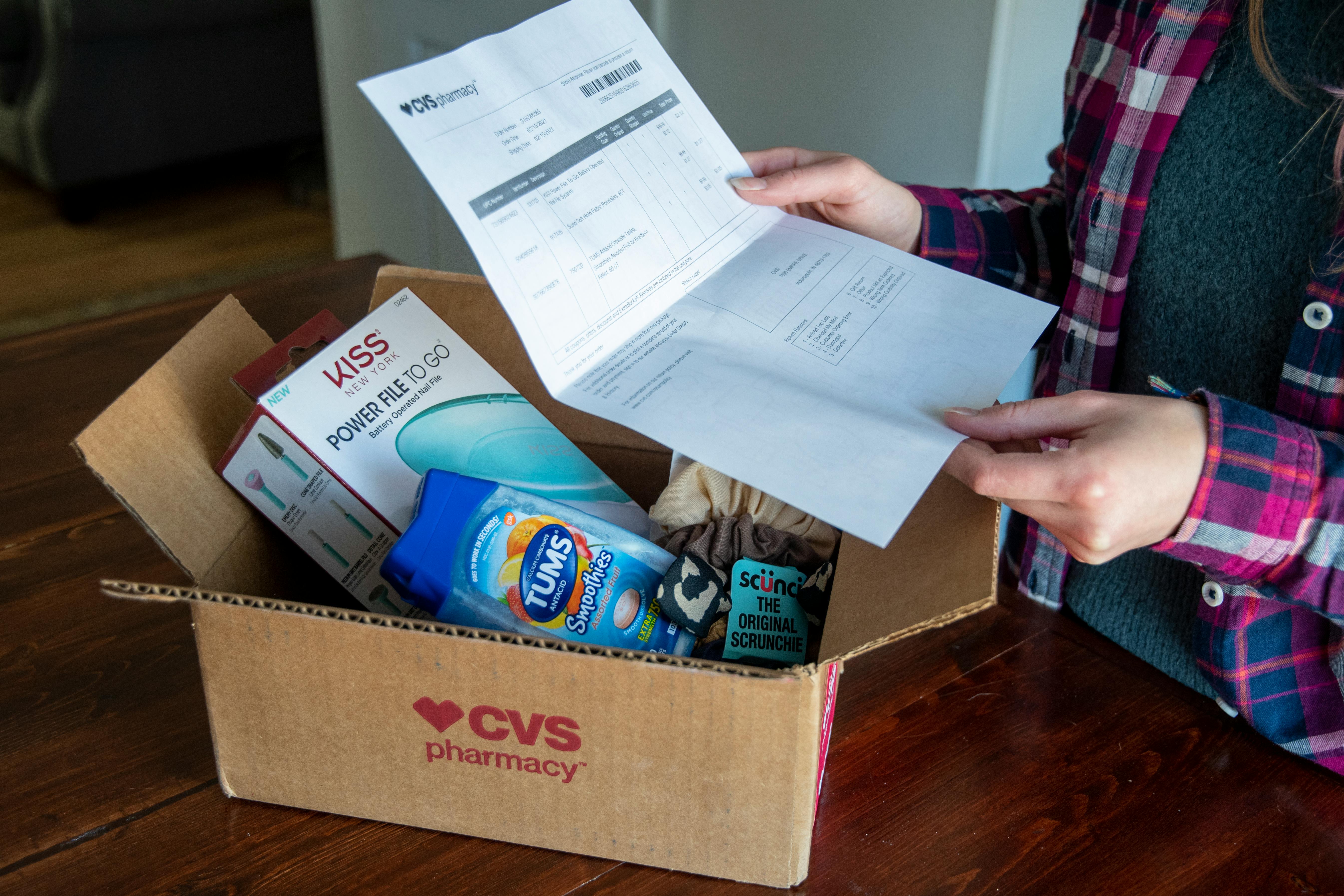 A person holding a cvs online order receipt over an open CVS box with products inside