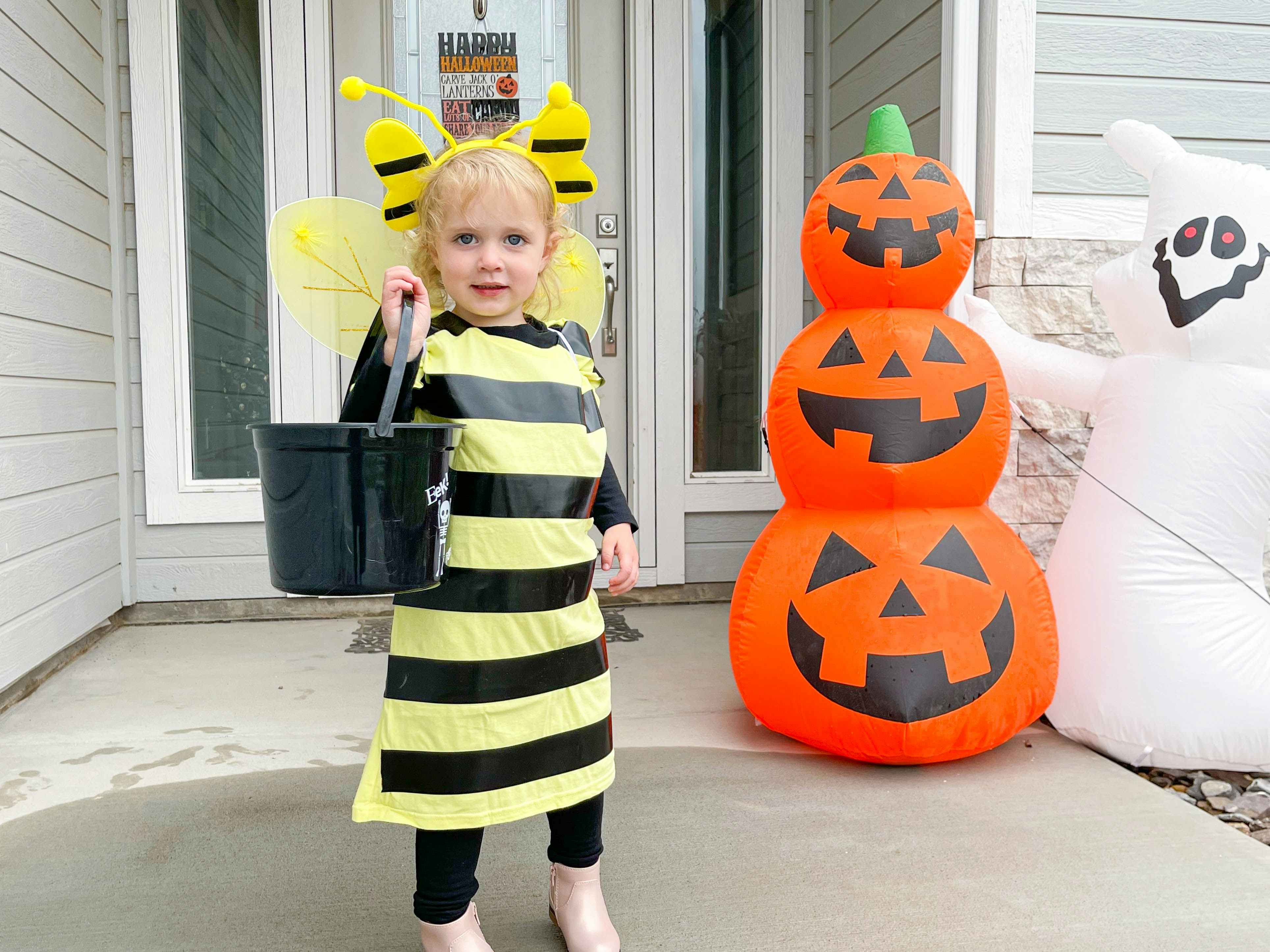 A little girl dressed as a bee standing on a front porch decorated for Halloween.