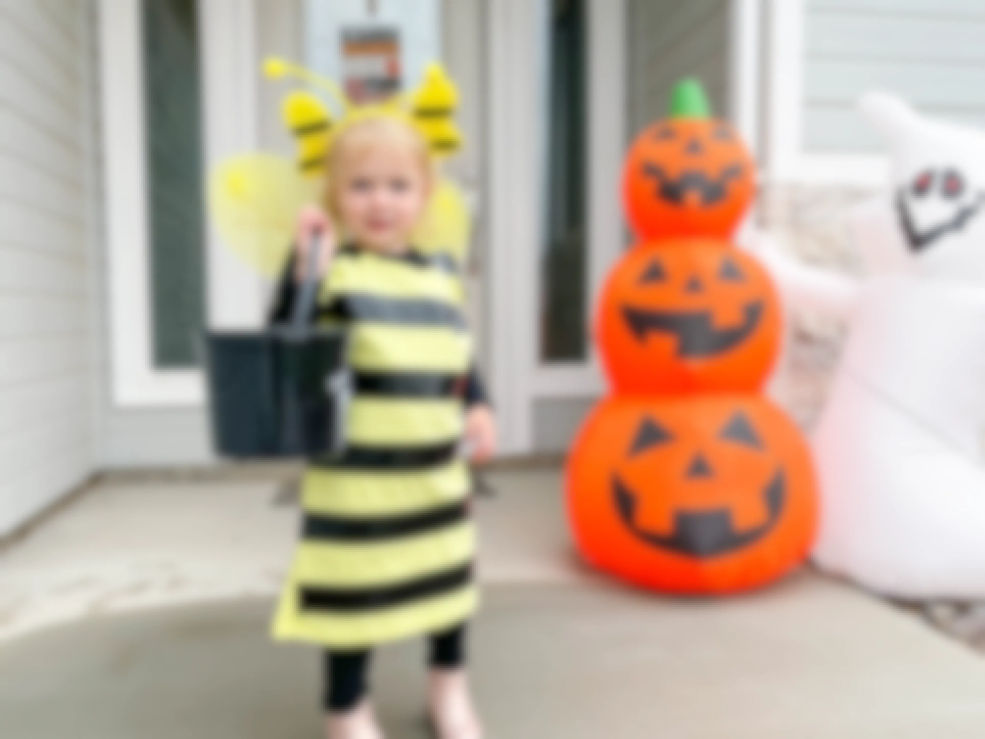 A little girl dressed as a bee standing on a front porch decorated for Halloween.