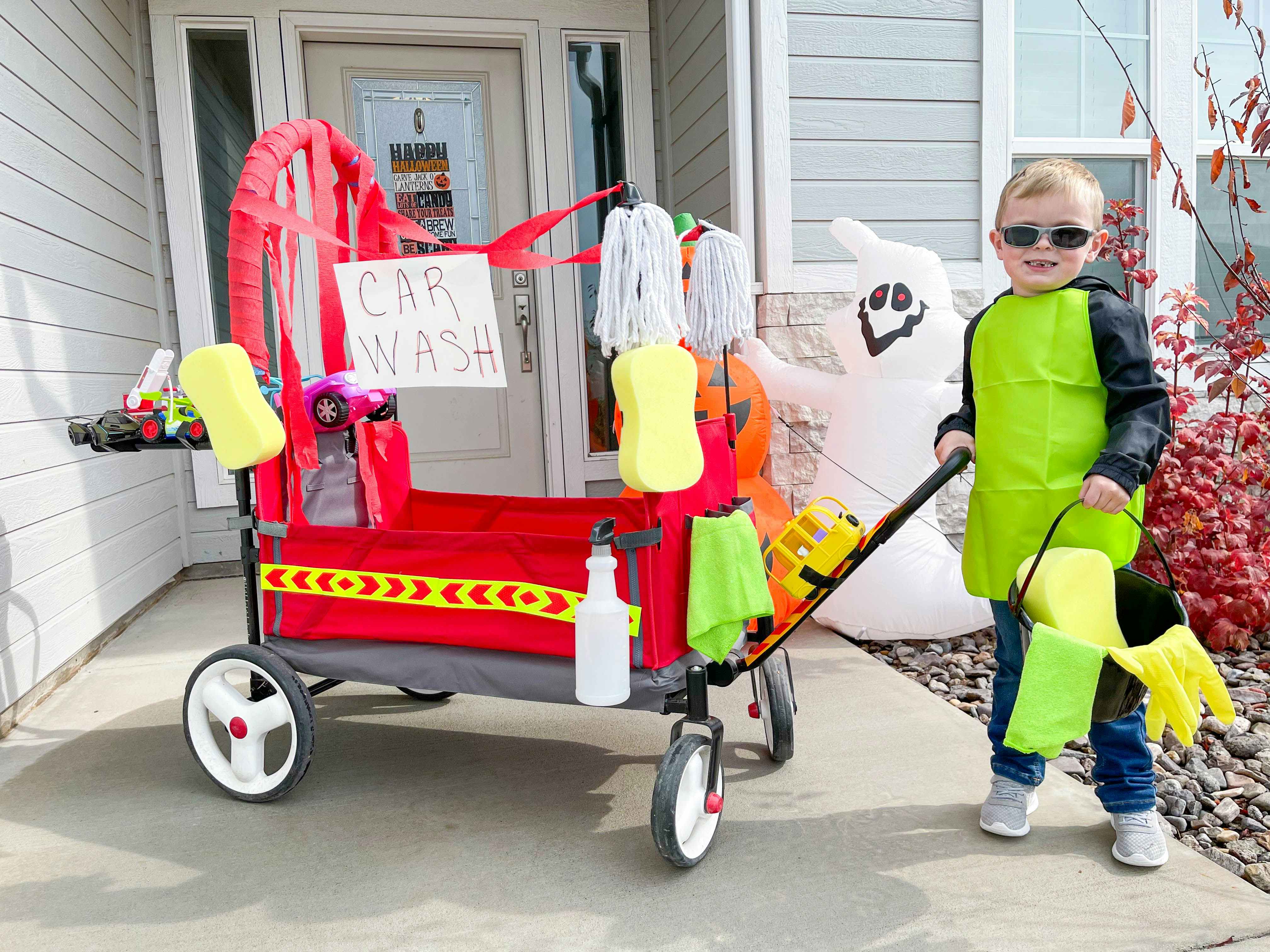 A boy wearing a car wash attendant costume using a wagon made up to look like a car wash.