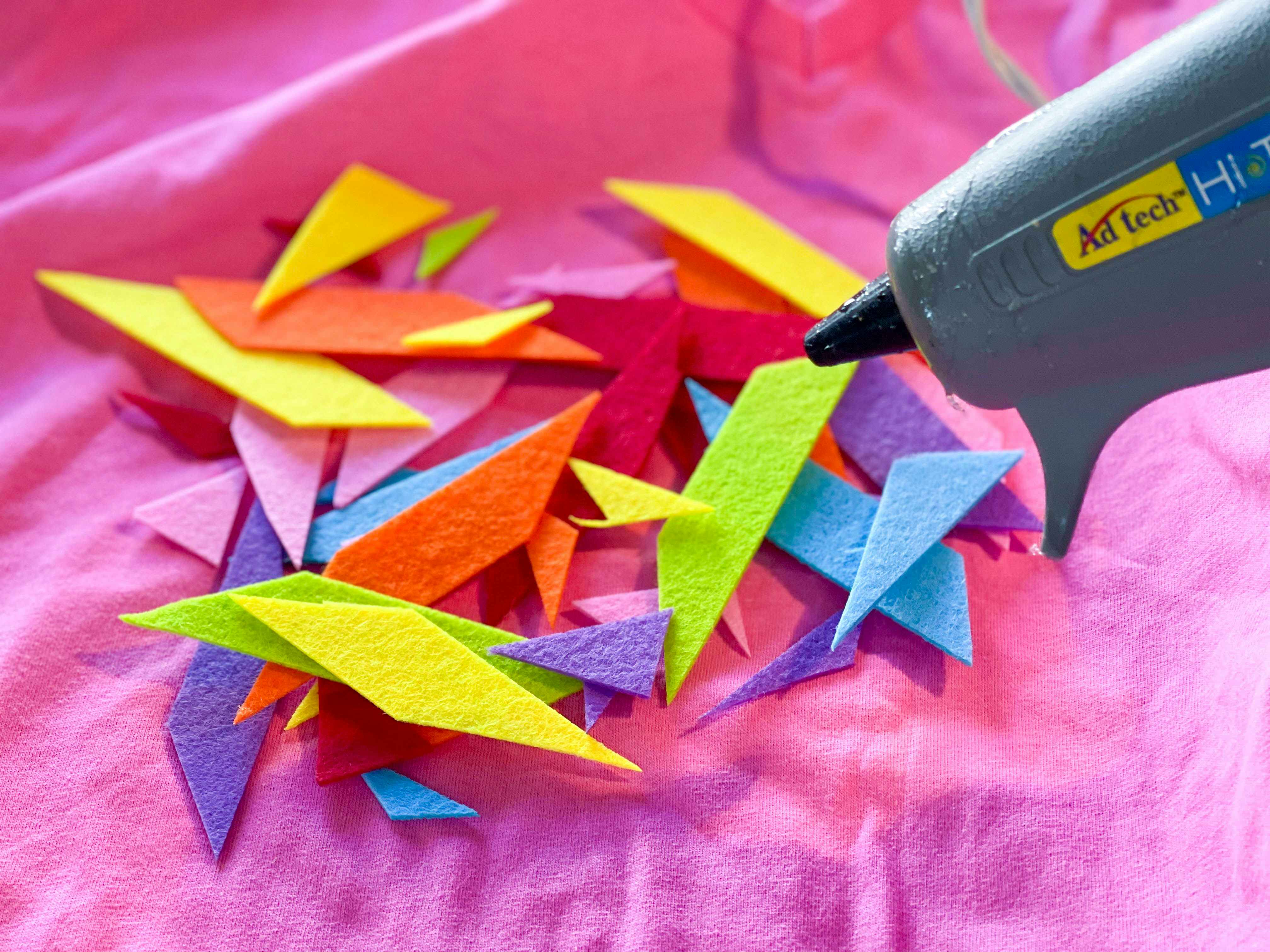 A hot glue gun near some cut-out shapes for sprinkles on a DIY ice cream cone costume.