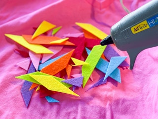 A hot glue gun near some cut-out shapes for sprinkles on a DIY ice cream cone costume.