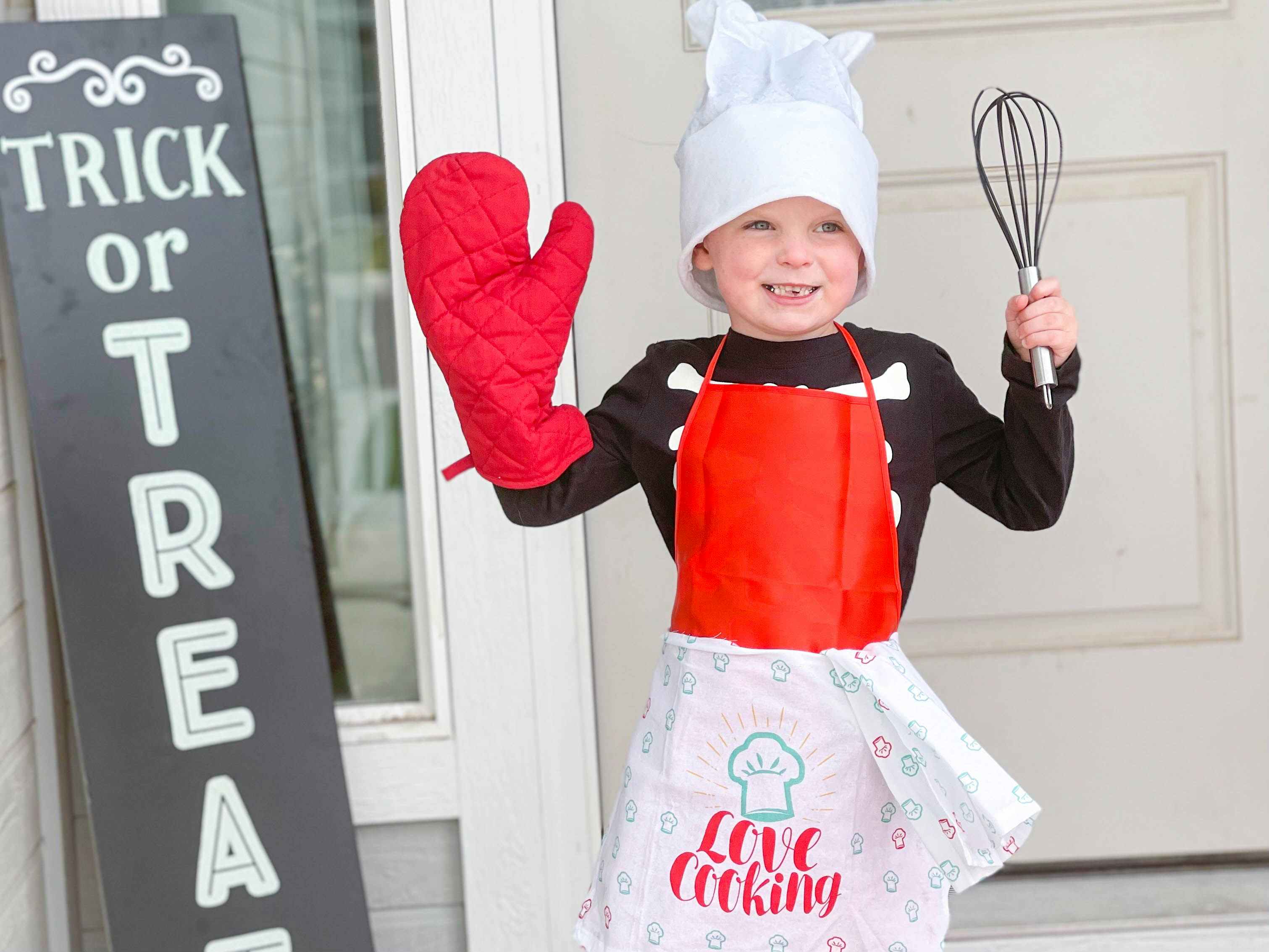 A kid in chef costume in front of door.