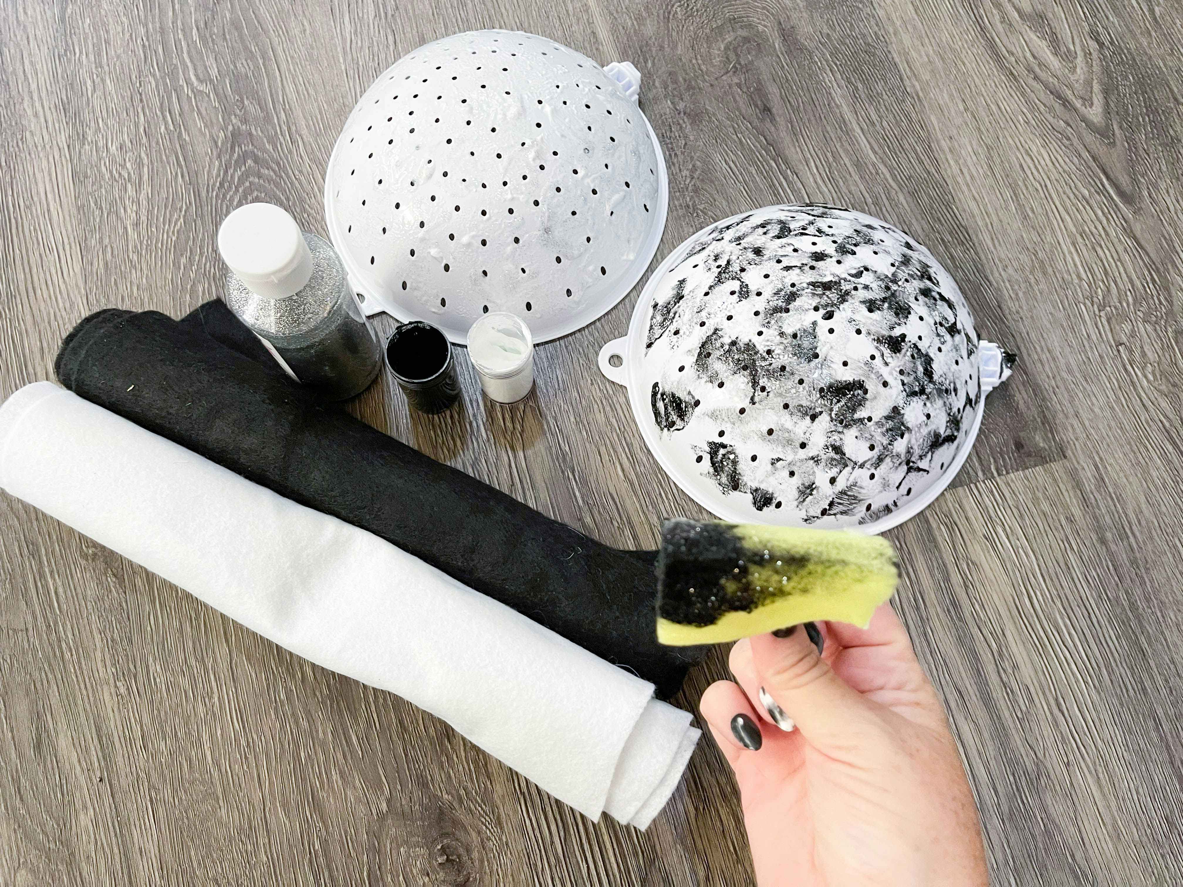 A person's hand holding a sponge with black paint on it in front of some materials for a DIY salt and pepper Halloween costume.