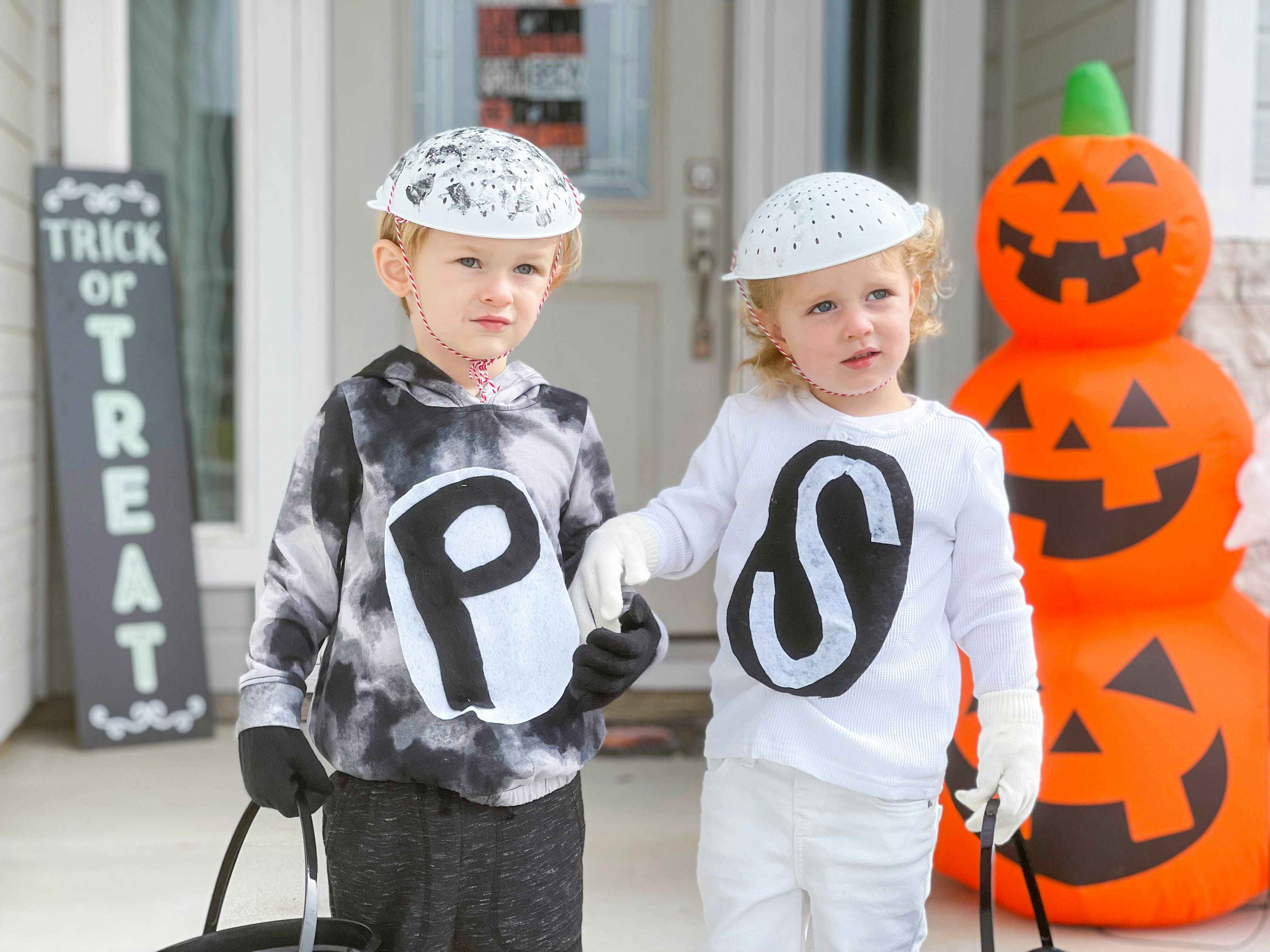 Two kids in salt and pepper costumes holding hands on the porch in front of some Halloween decorations.