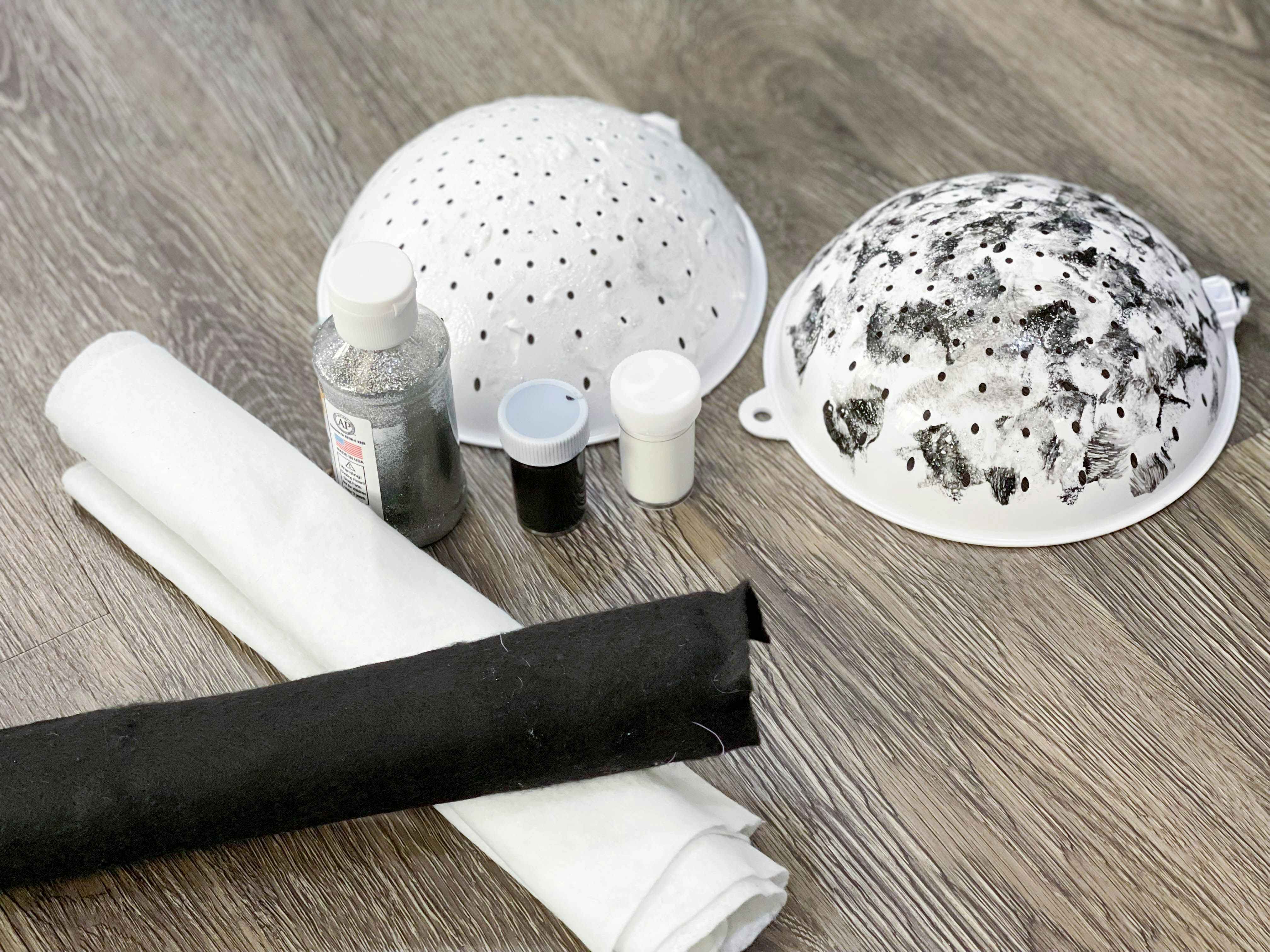 black and white felt, paint and painted colanders set up on the floor
