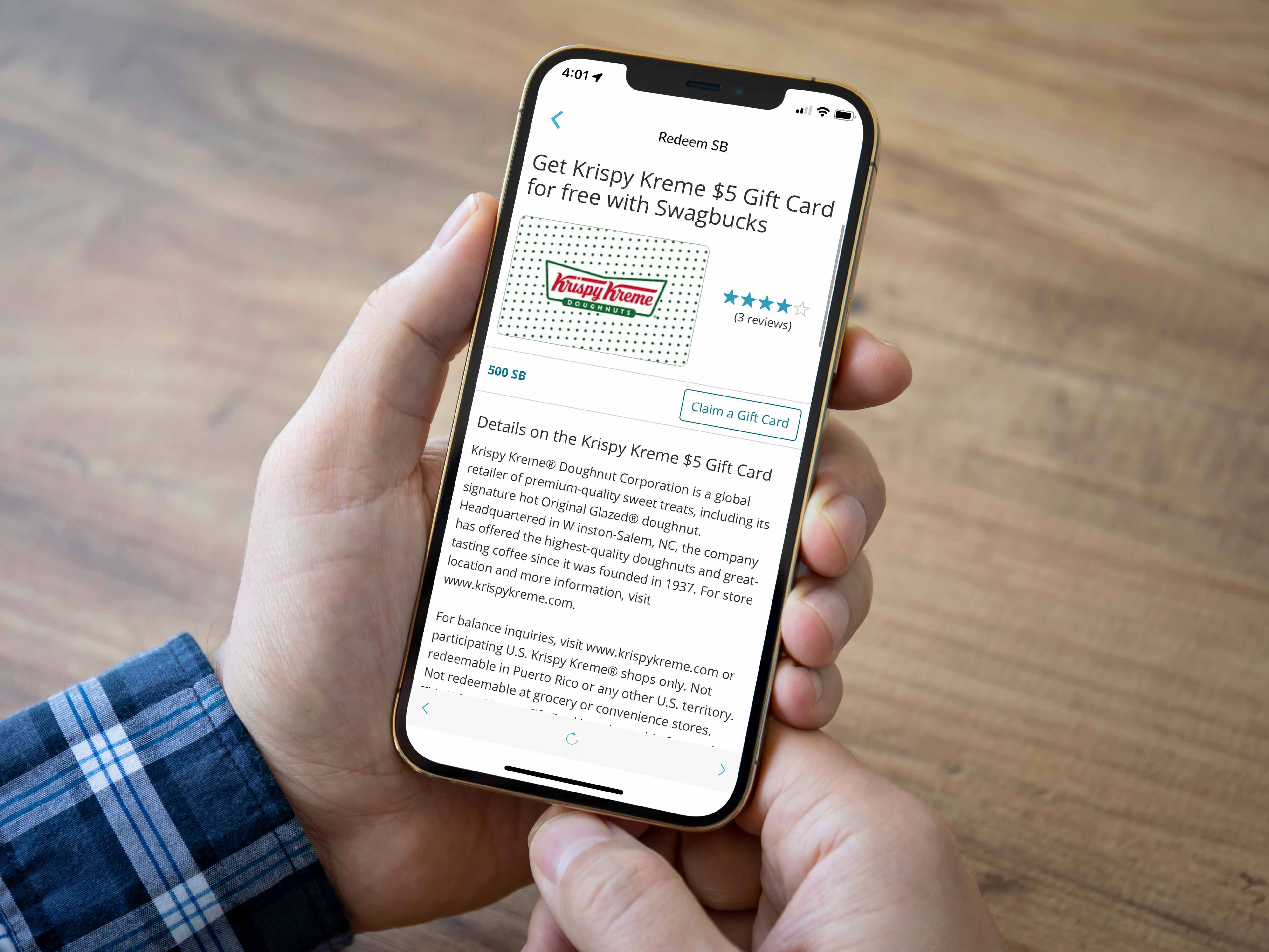 A person's hands holding a cell phone displaying the page for a $5 Krispy Kreme gift card reward on the Swagbucks app