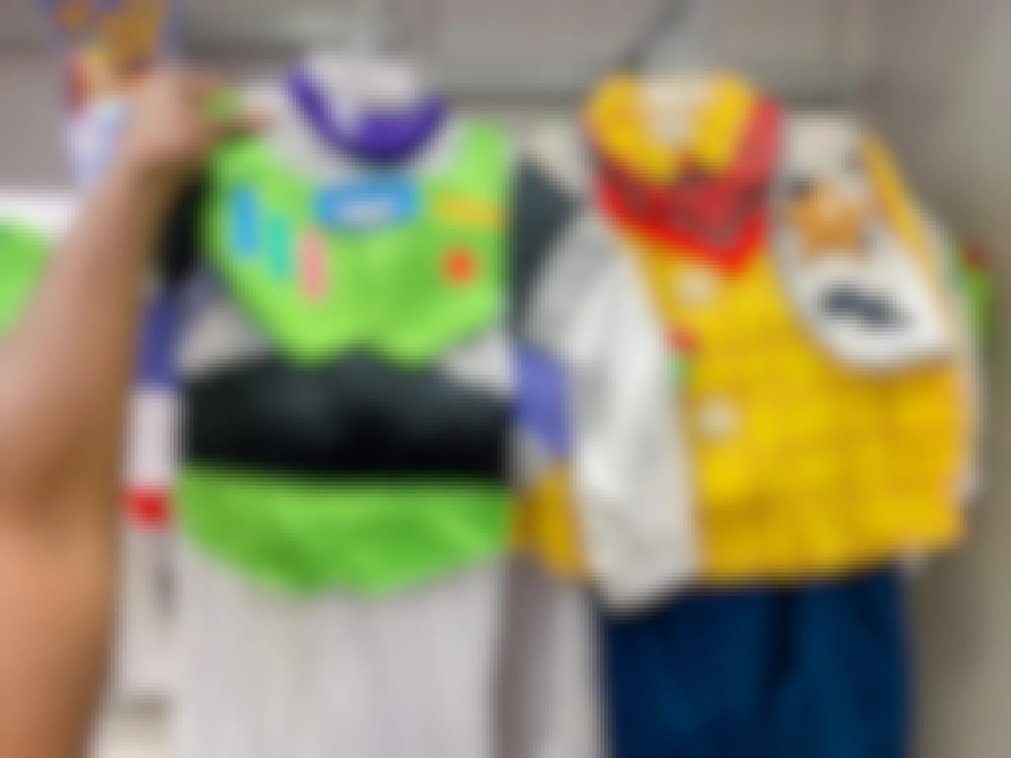 A person's hand holding up a Buzz Lightyear costume next to a Woody costume.