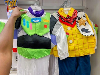 A person's hand holding up a Buzz Lightyear costume next to a Woody costume.