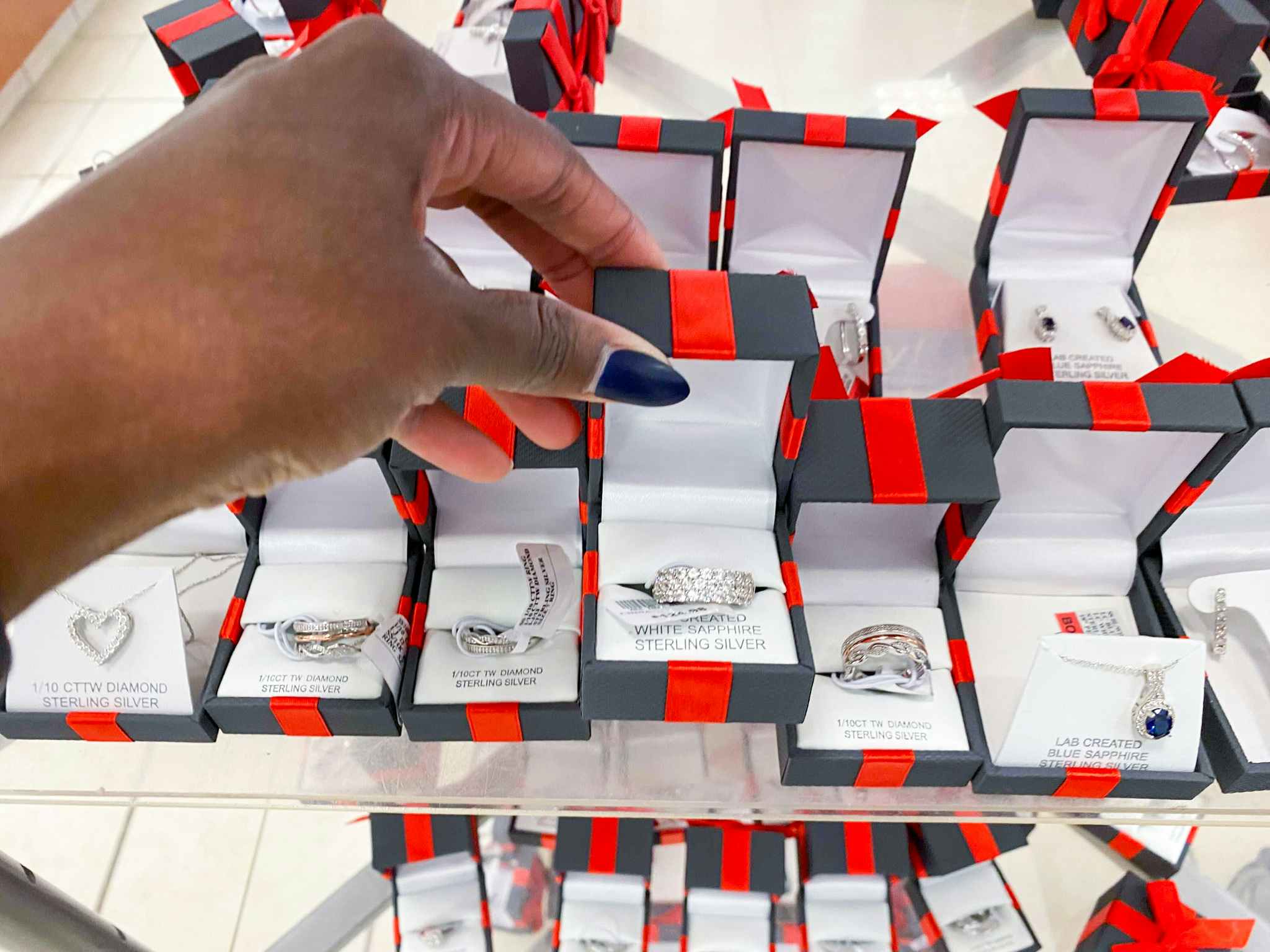 A person's hand picking up a ring in a box from a display of jewelry at JCPenney.