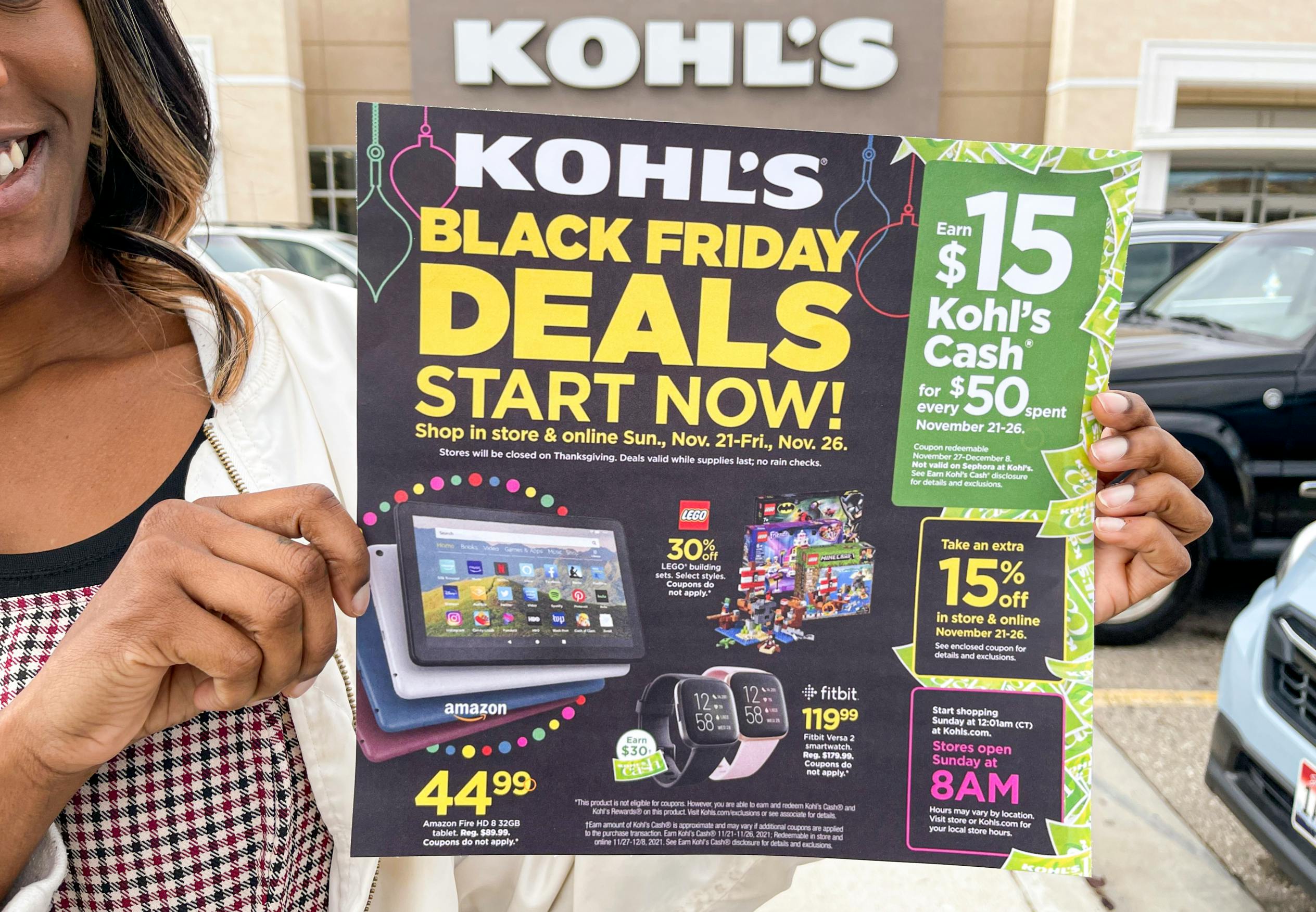 A woman holding a Kohl's Black Friday ad in front of a Kohl's storefront.