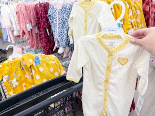 Yellow carter baby sleepers in a cart. A person is holding one up next to the cart.