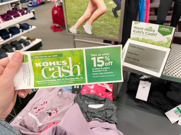 A person holding Kohl's cash near a sales sign