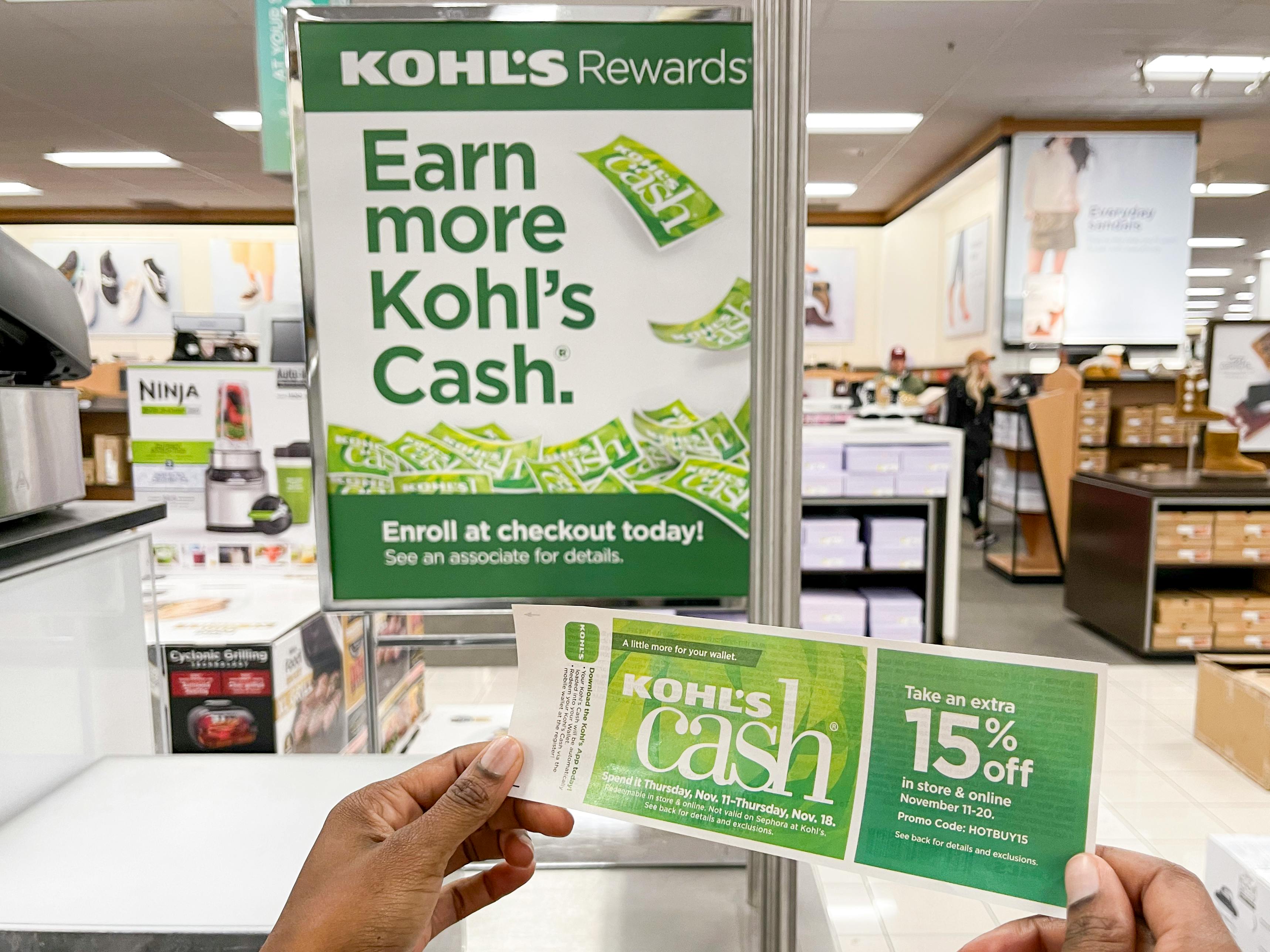 A person holding Kohl's Cash near a Kohl's Cash sign inside Kohl's.