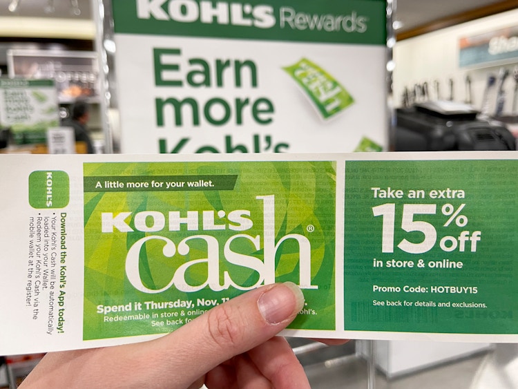A person holding Kohl's Cash in front of a Kohl's Rewards sign.