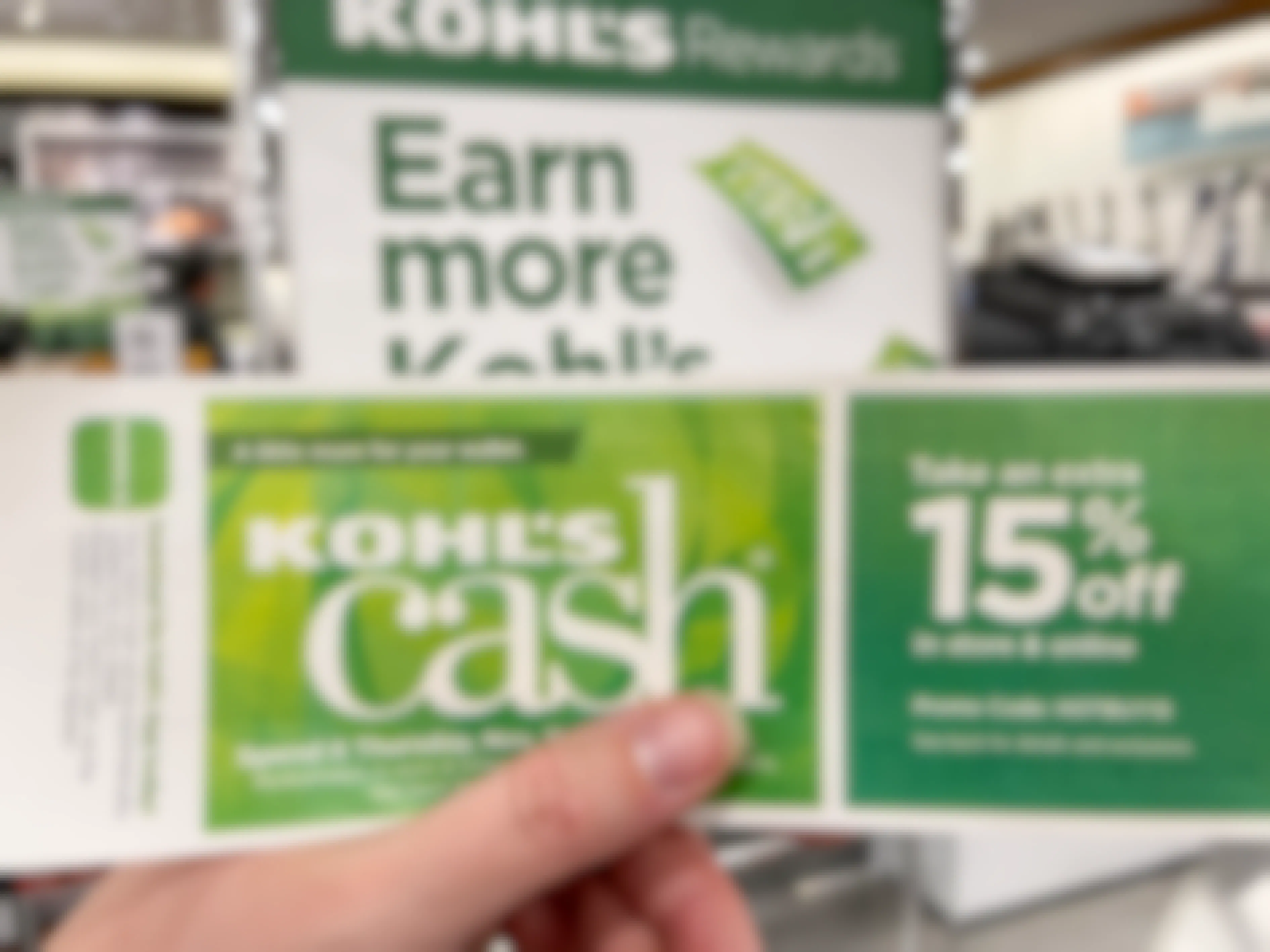 A person holding Kohl's Cash in front of a Kohl's Rewards sign.