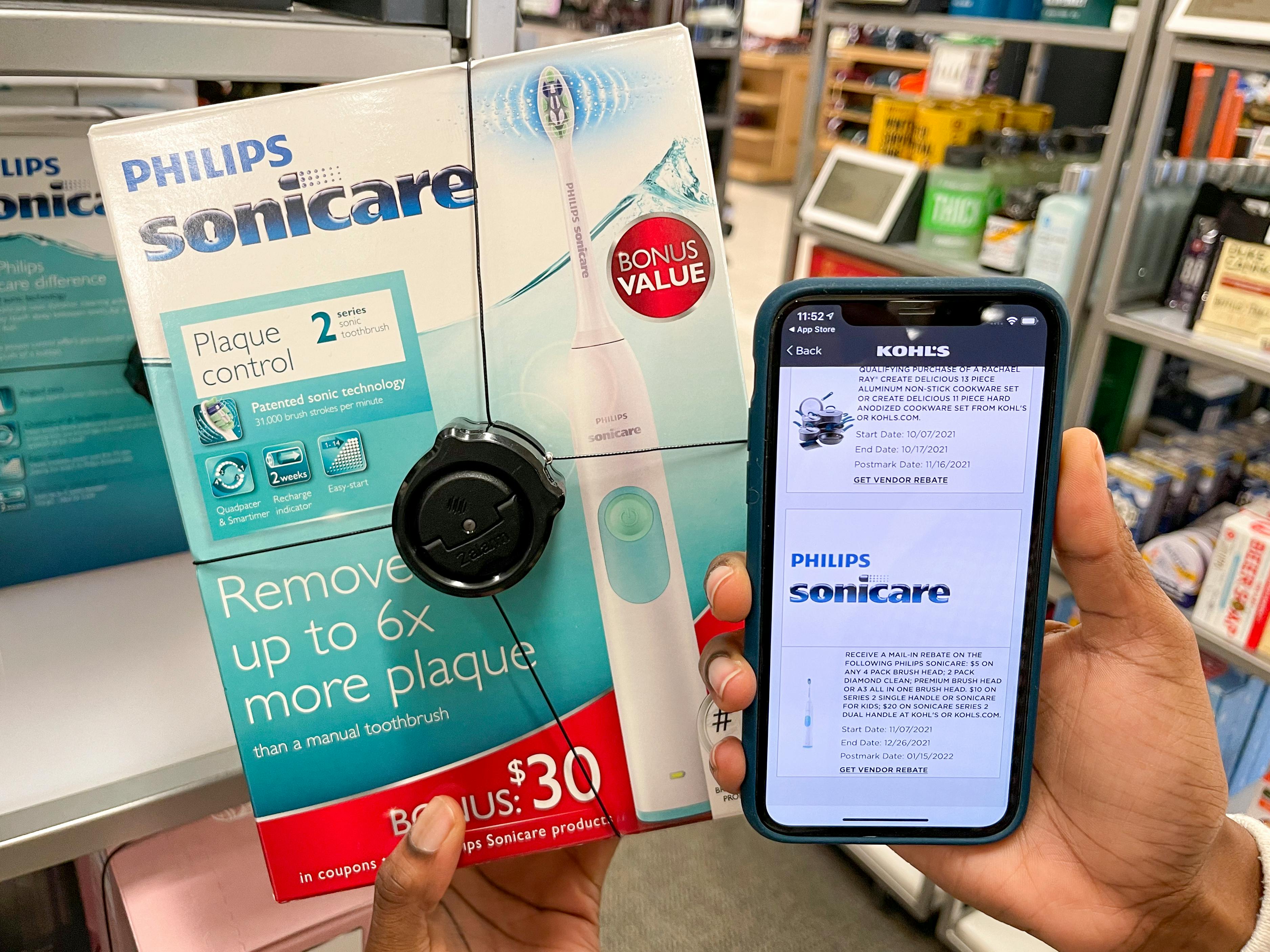 A cell phone displaying a Sonicare toothbrush rebate being held next to a Sonicare toothbrush box in Kohl's..