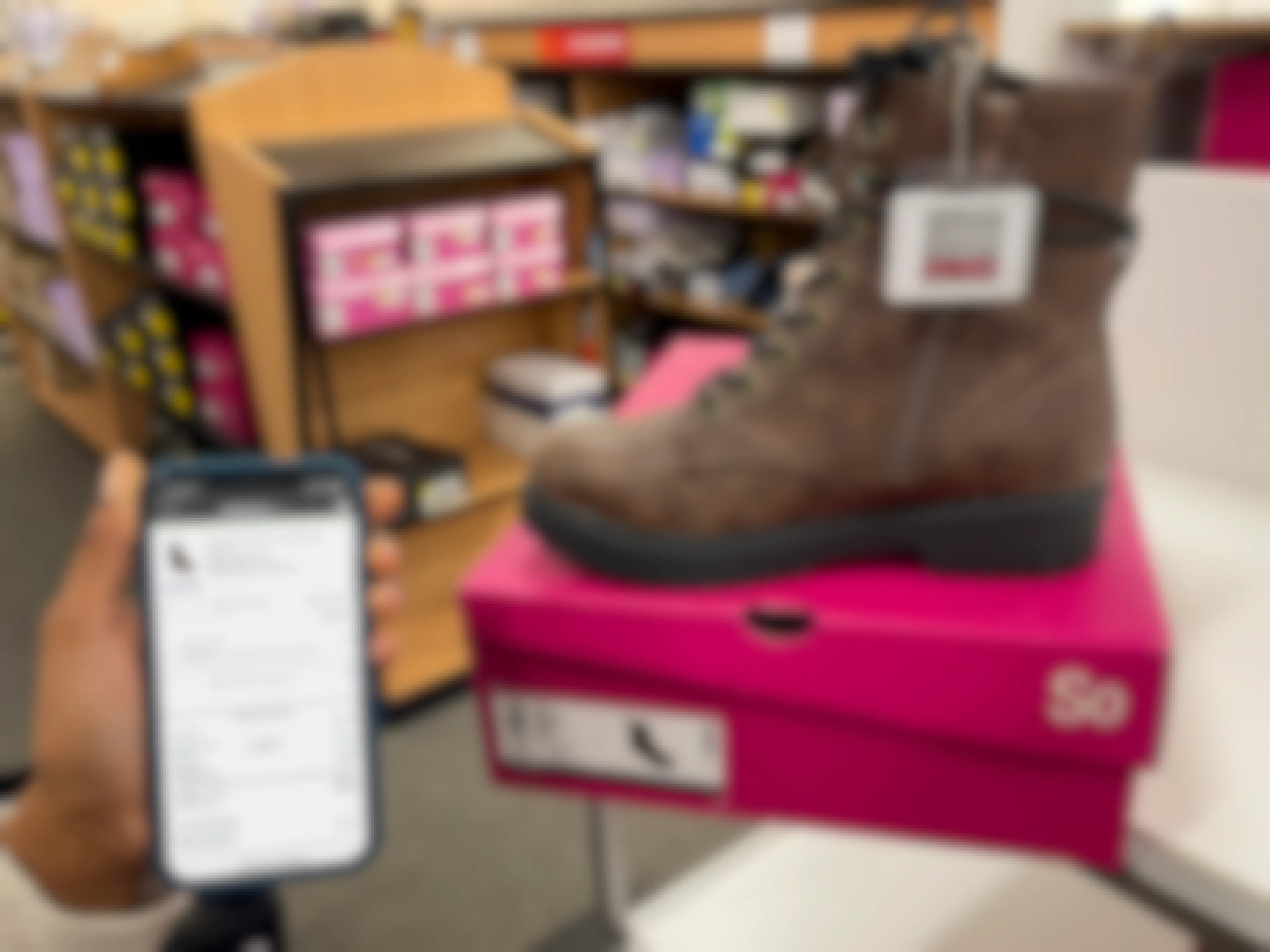 A cell phone held next to a hair of womens boots with a sales tag
