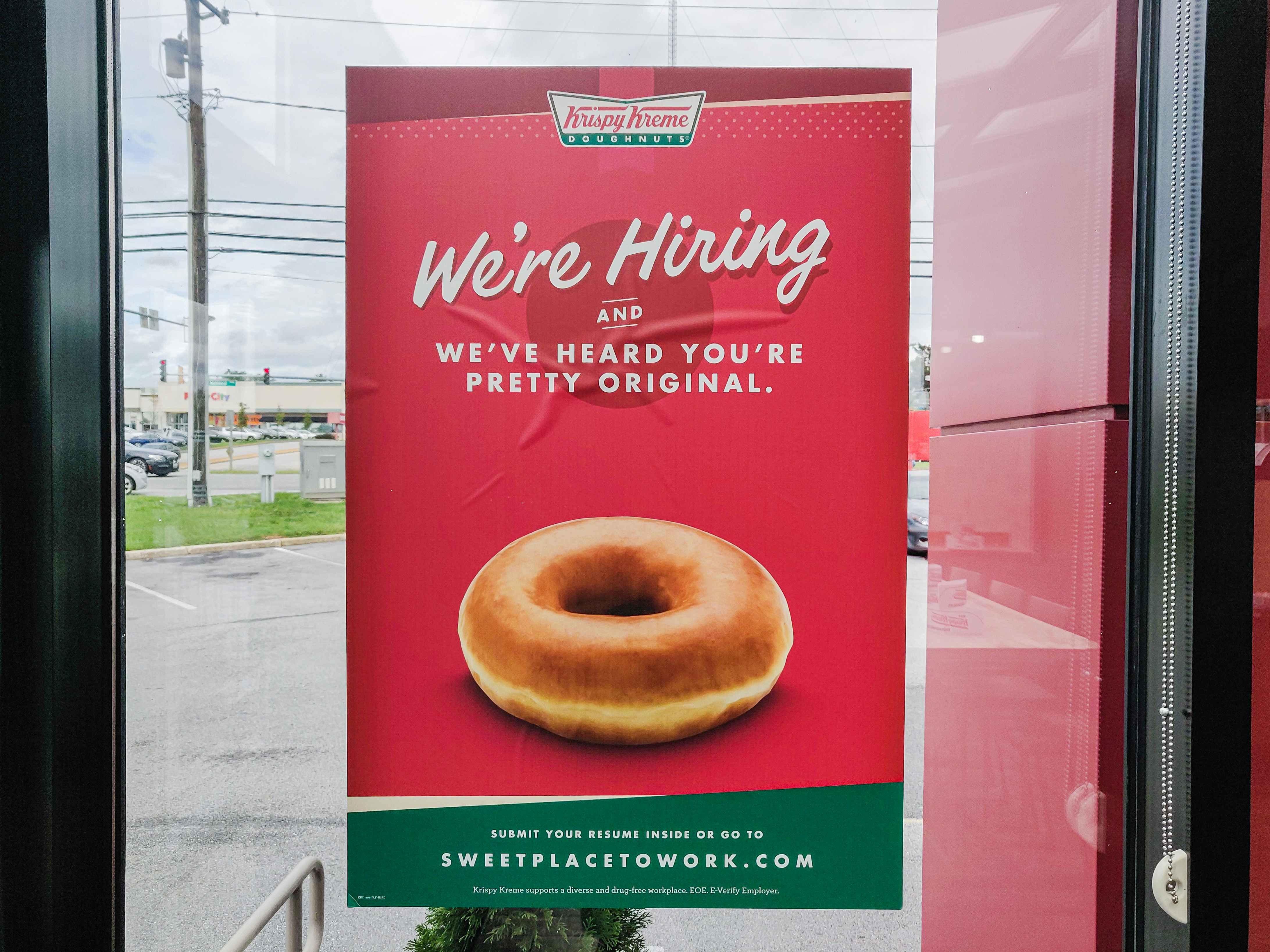 A "We're Hiring" sign on a Krispy Kreme door.