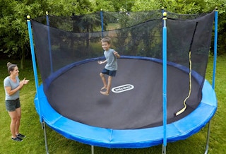 A child jumping on a Little Tikes brand trampoline in the backyard while the mom watches and smiles.