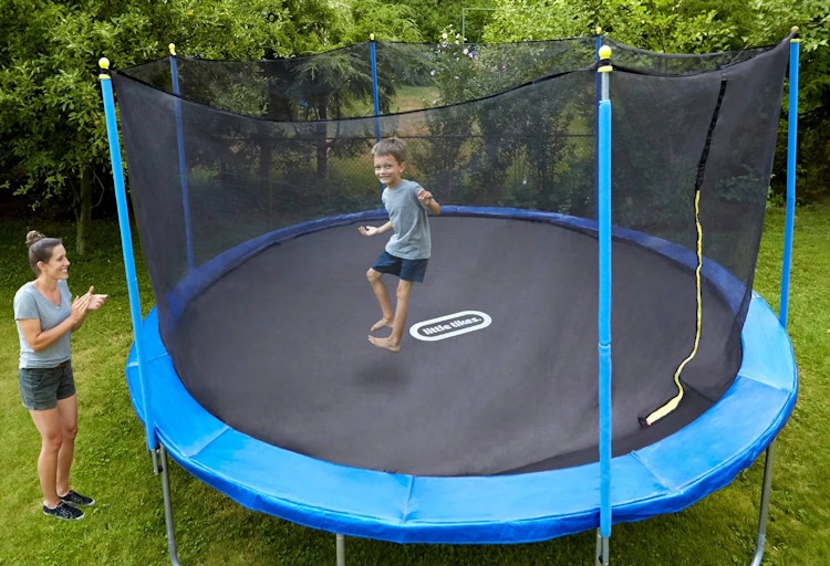 A child jumping on a Little Tikes brand trampoline in the backyard while the mom watches and smiles.