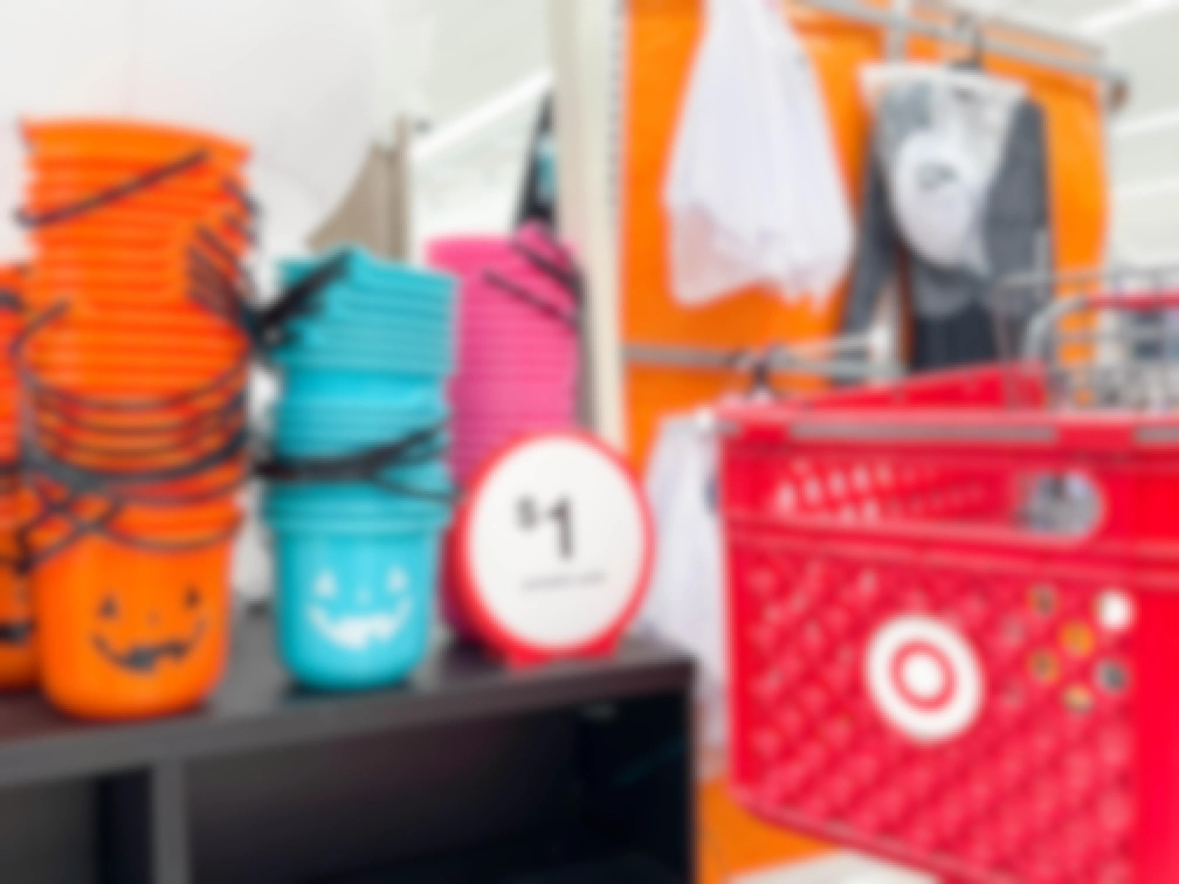 a target shopping cart parked next to a display shelf with orange, blue and pink halloween pails next to a sign that says $1