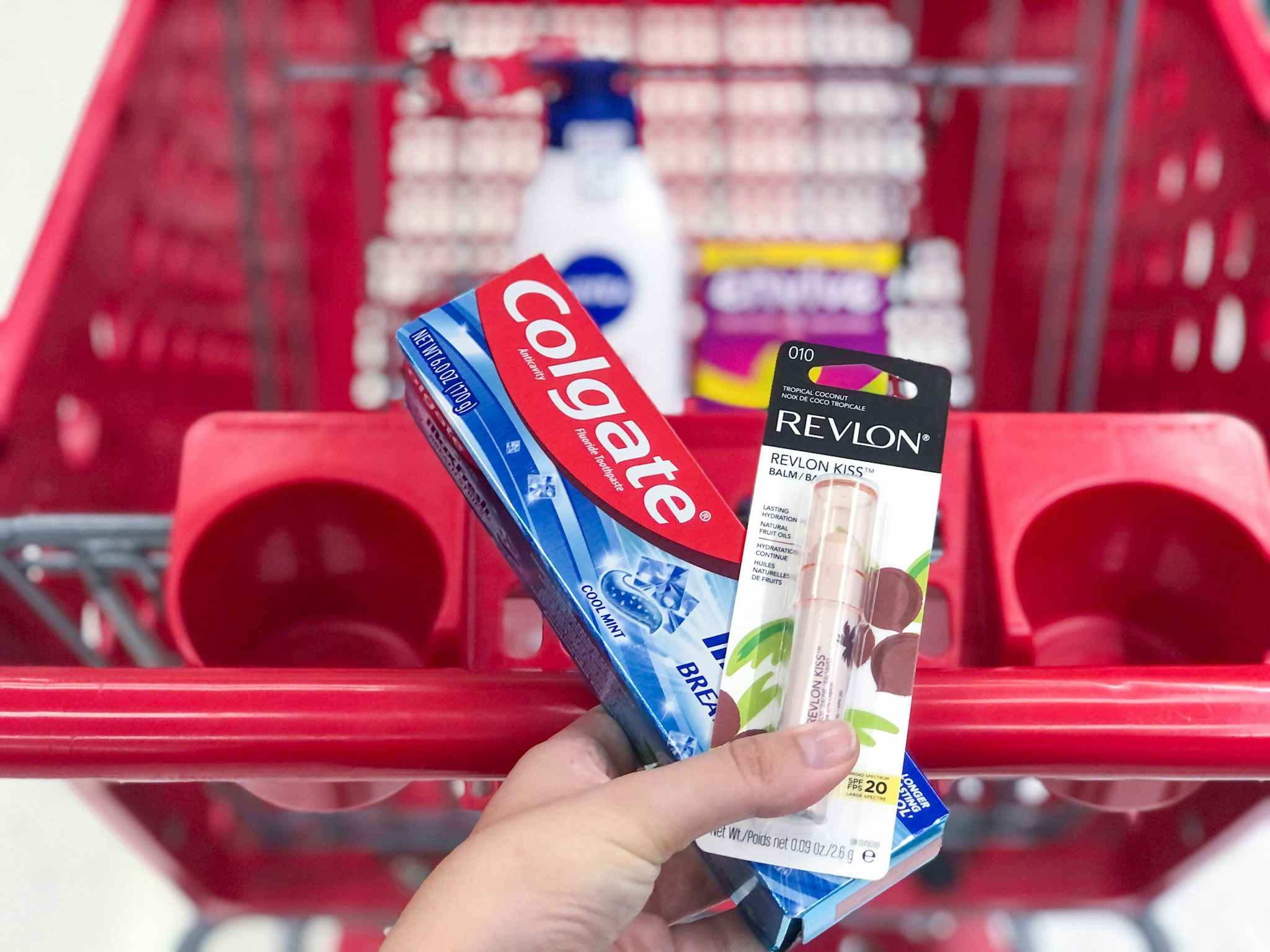 hand holding colgate and revlon over a target cart