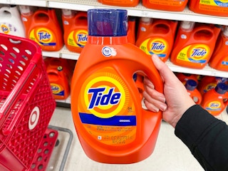 A hand holding Tide liquid laundry detergent in a store aisle.