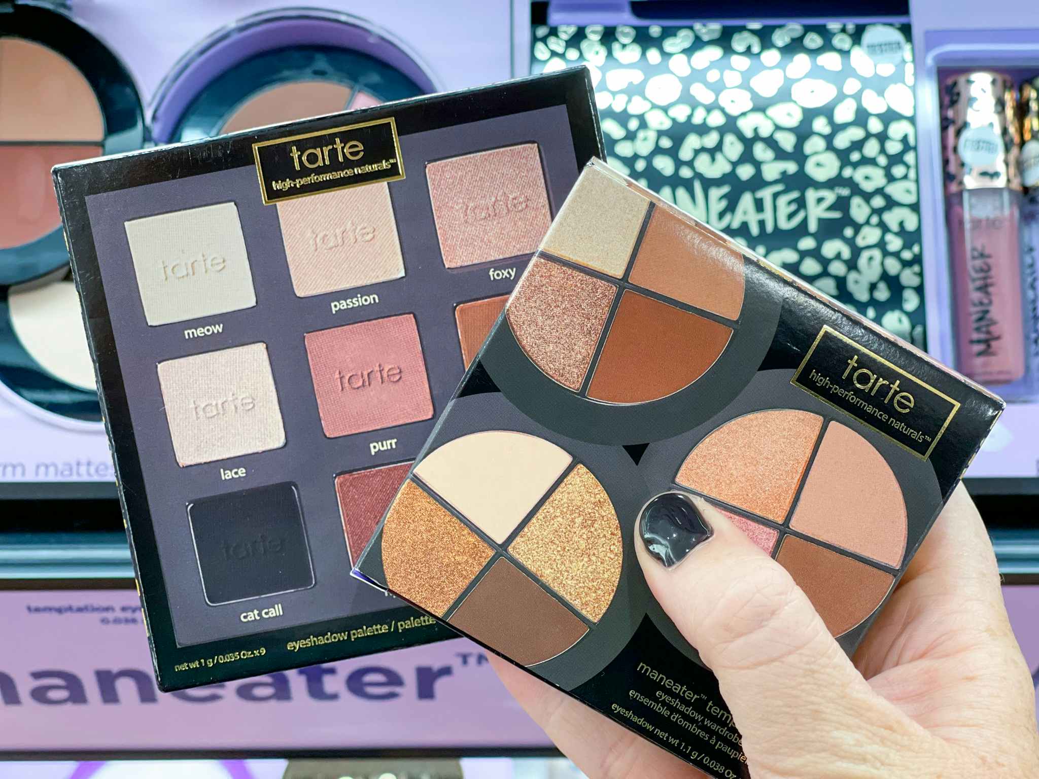 hand holding tarte eyeshadow palettes in front of a Tarte display.