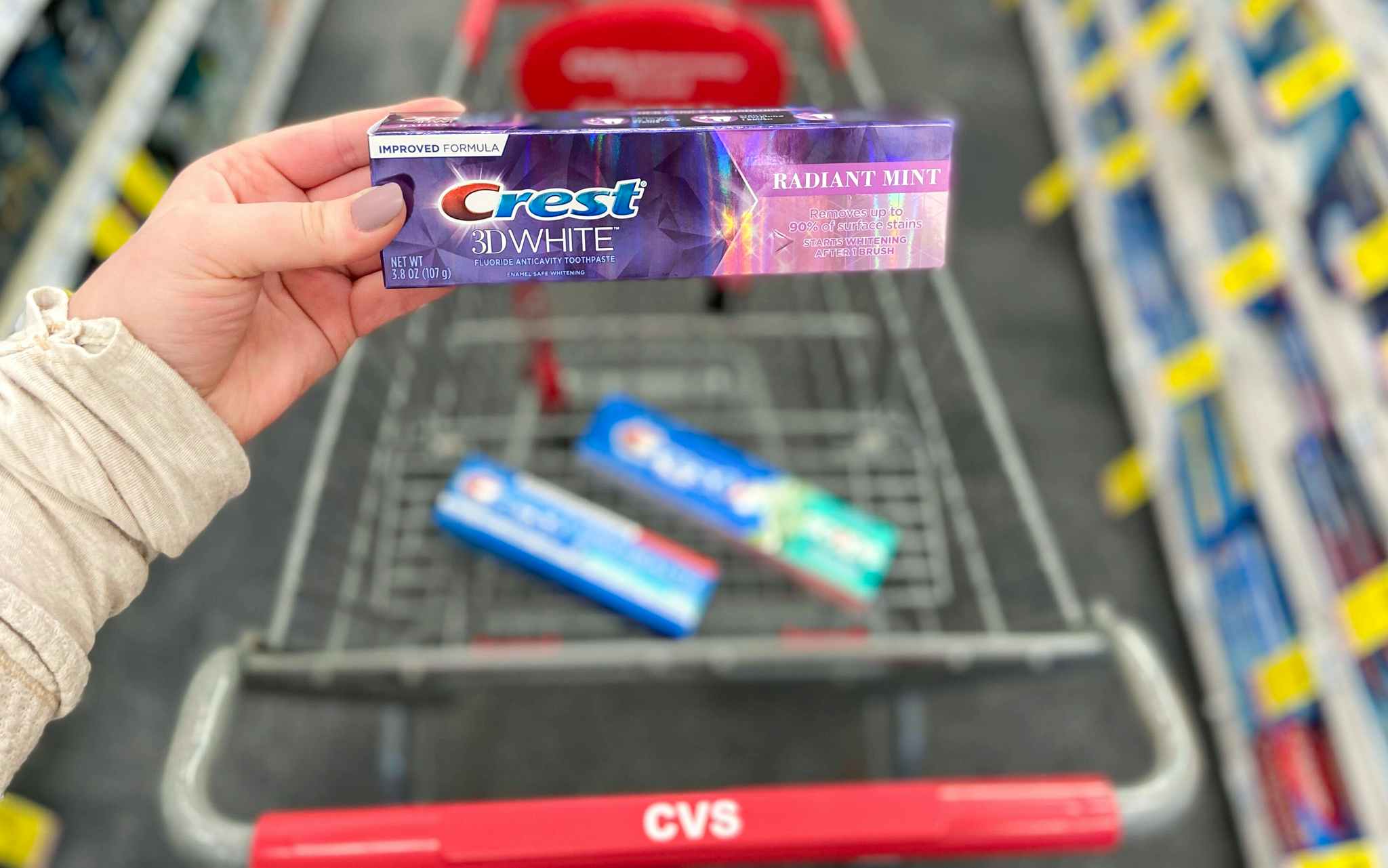 someone holding crest toothpaste next to cvs cart