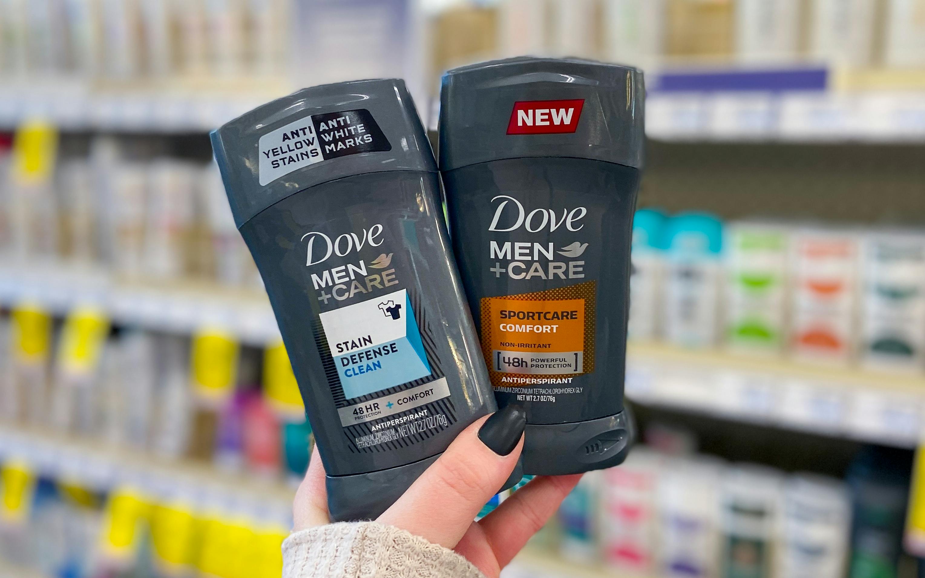 A person holding up two sticks of Dove Men +Care antiperspirant deodorant. One is Stain Defense Clean and the other is Sportcare Comfort.