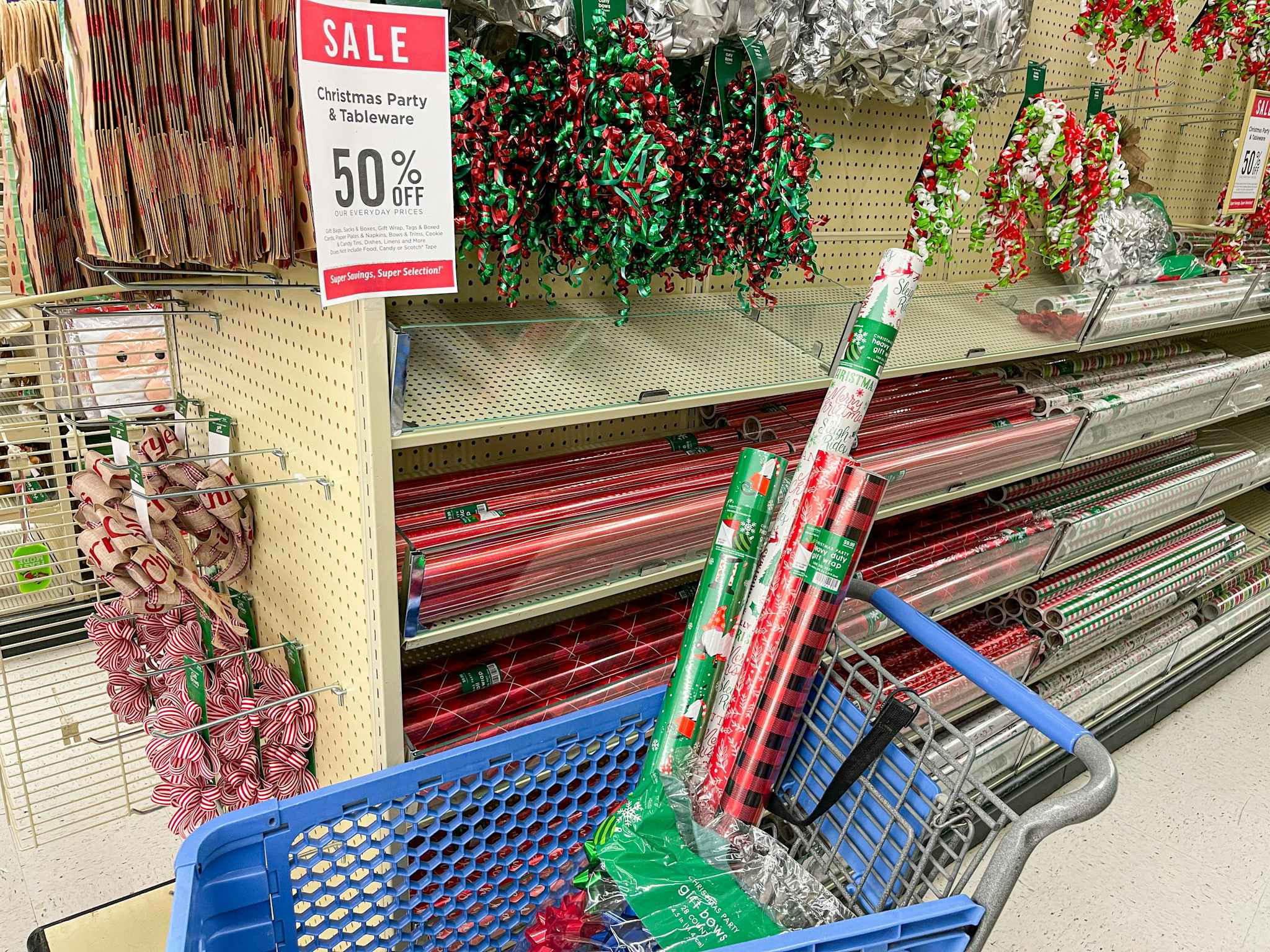 Rolls of gift wrapping paper and other supplies in a Hobby Lobby shopping cart next to a sign advertising 50% off