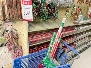 Rolls of gift wrapping paper and other supplies in a Hobby Lobby shopping cart next to a sign advertising 50% off