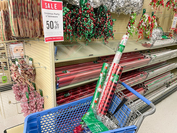 Rolls of gift wrapping paper and other supplies in a Hobby Lobby shopping cart next to a sign advertising 50% off