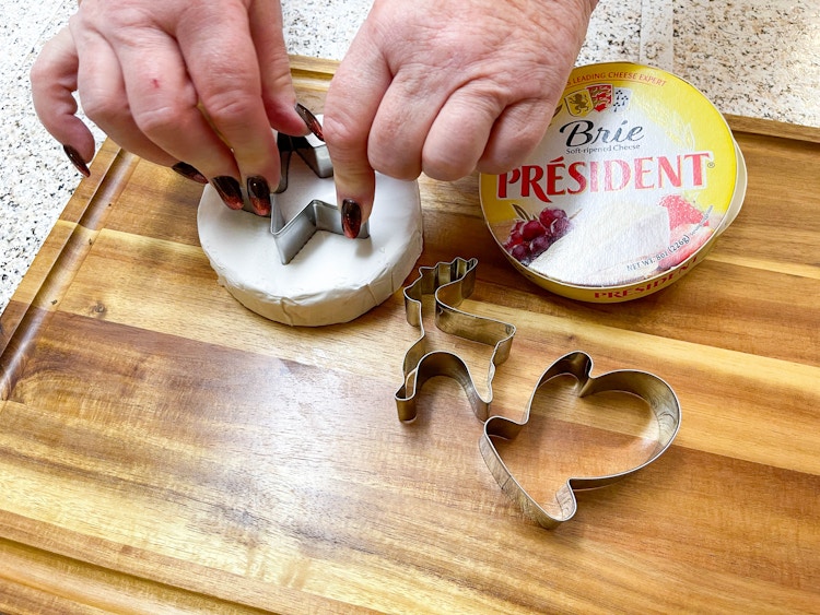 charcuterie board with woman cutting brie with cookie cutters 