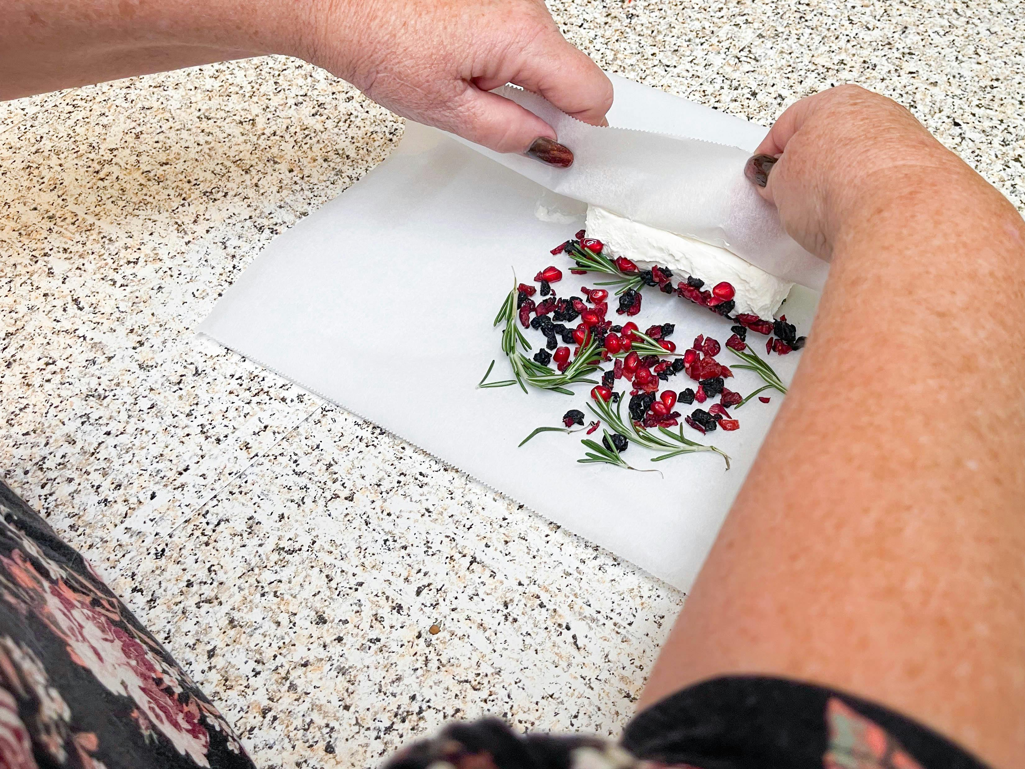 woman rolling goat cheese in rosemary & dried fruits with wax paper 