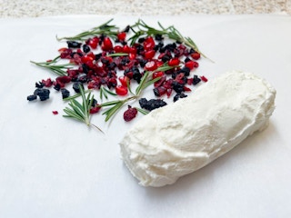 woman rolling goat cheese in rosemary & dried fruits with wax paper 