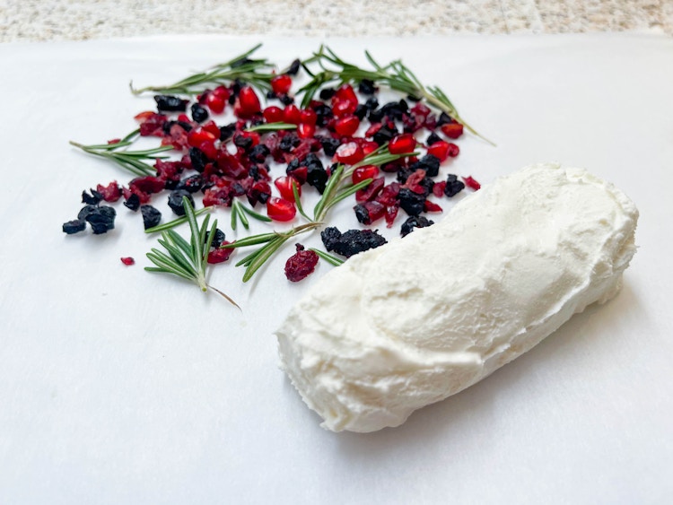 woman rolling goat cheese in rosemary & dried fruits with wax paper 