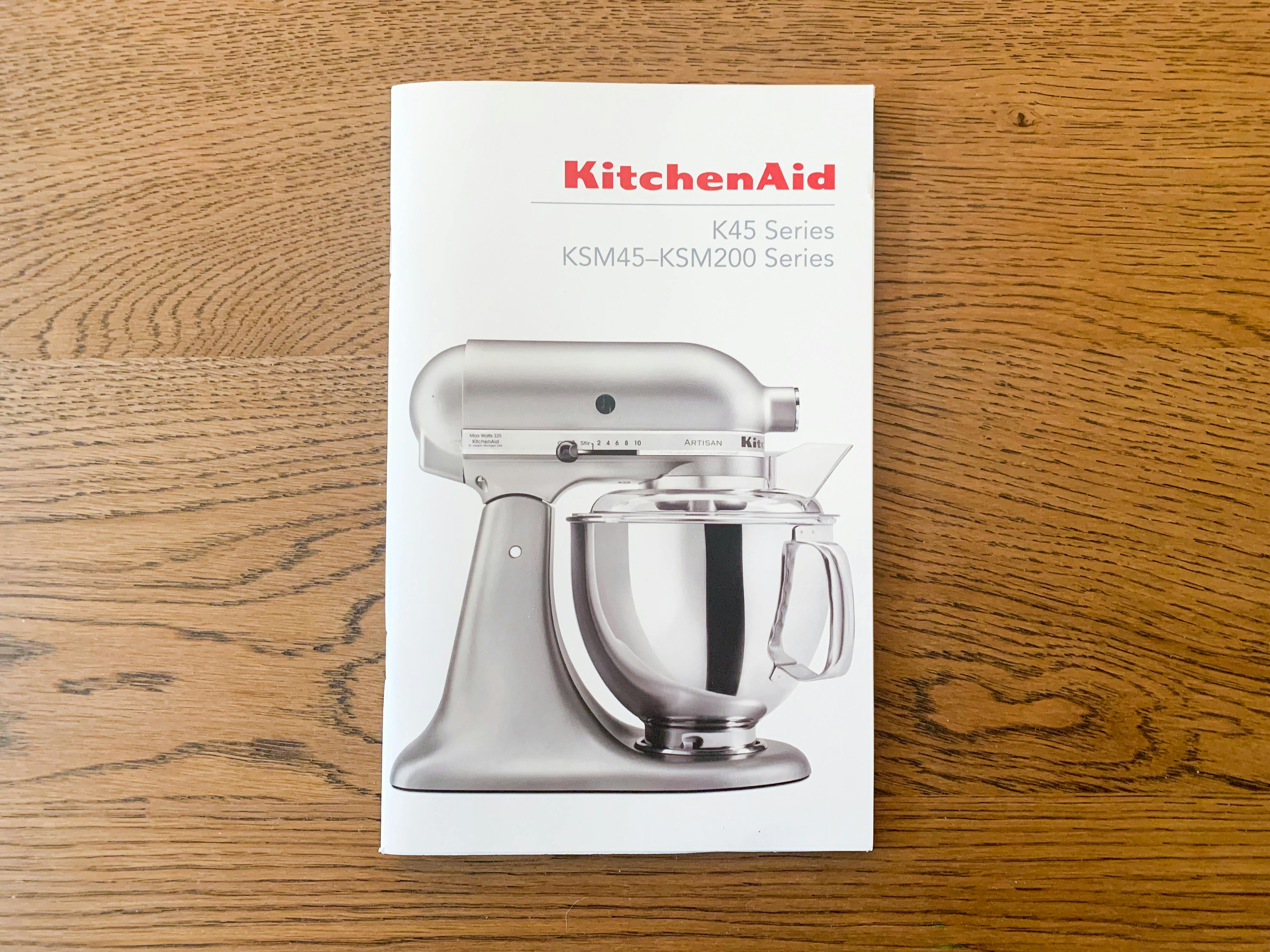 the front cover of the KitchenAid Mixer manual on a wood table
