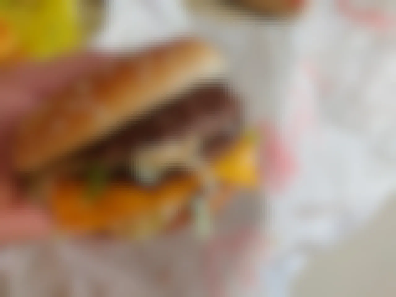 A person's hand holding a burger from McDonald's above the paper wrapper on the table.