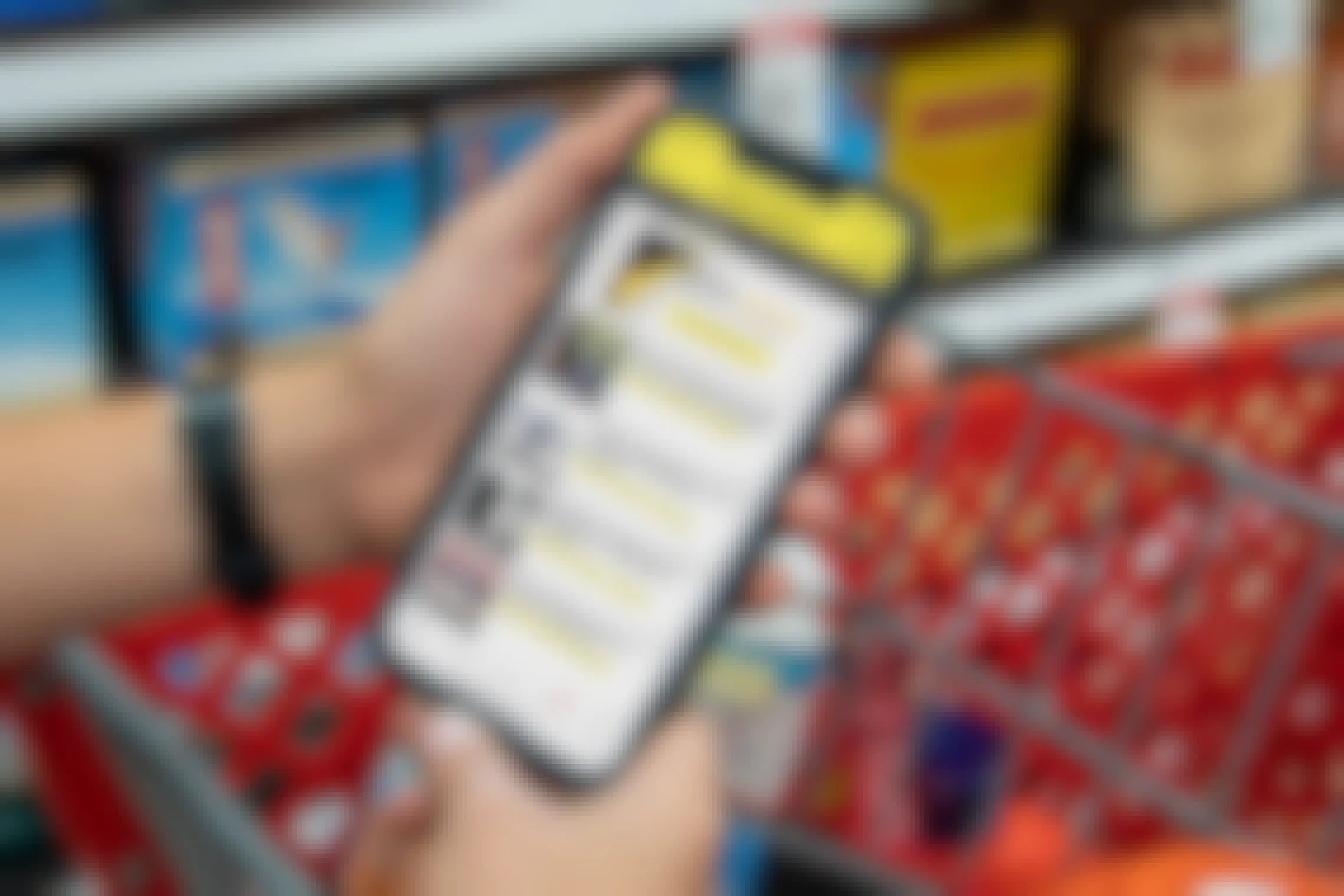 A person's hands resting on a shopping cart, holding a cell phone displaying the KCL app's Black Friday deals.