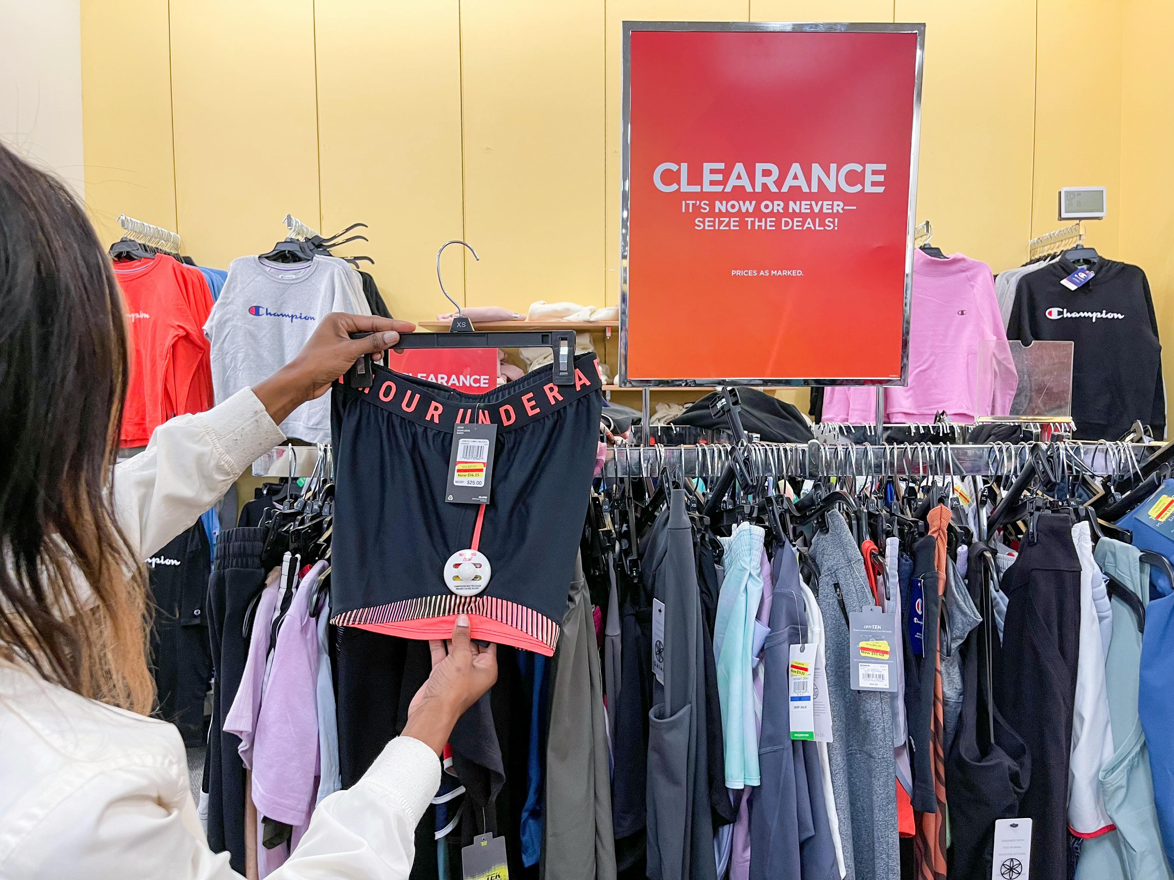 A woman holding a pair of Under Armour shorts next to a clearance sign