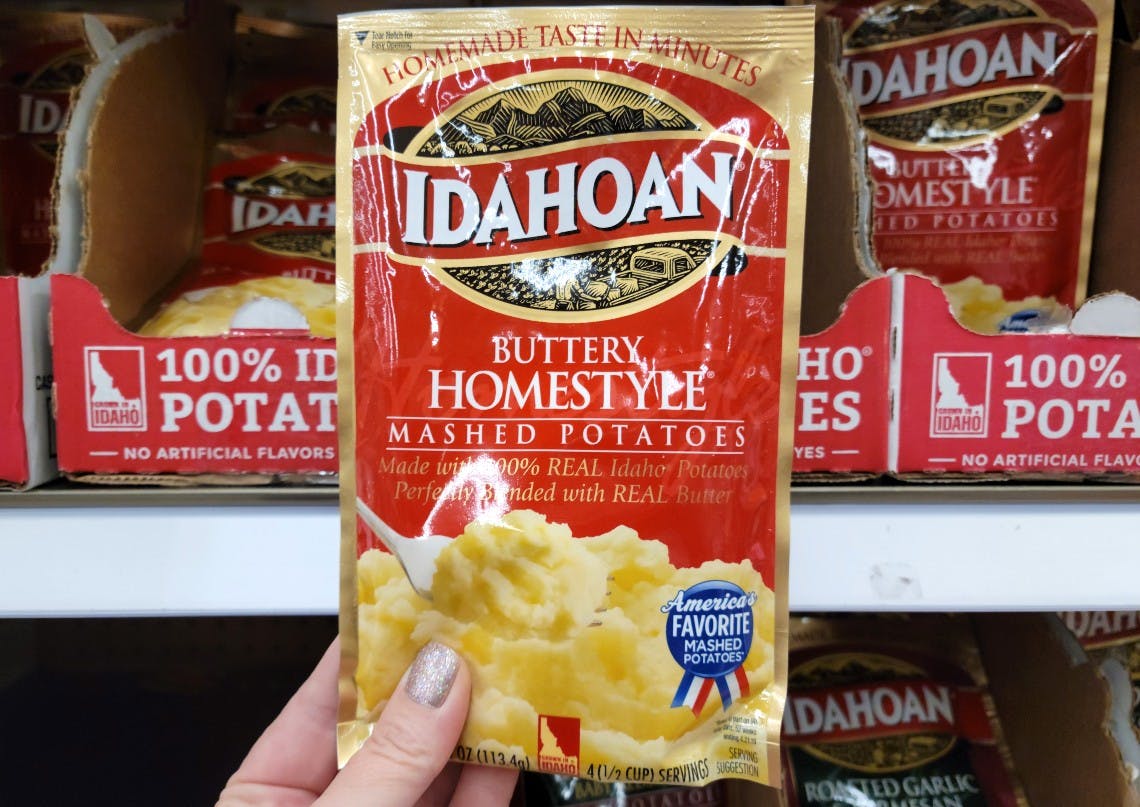 A person holding a packet of Idahoan instant potatoes in front of a store shelf with other packets of Idahoan instant potatoes.