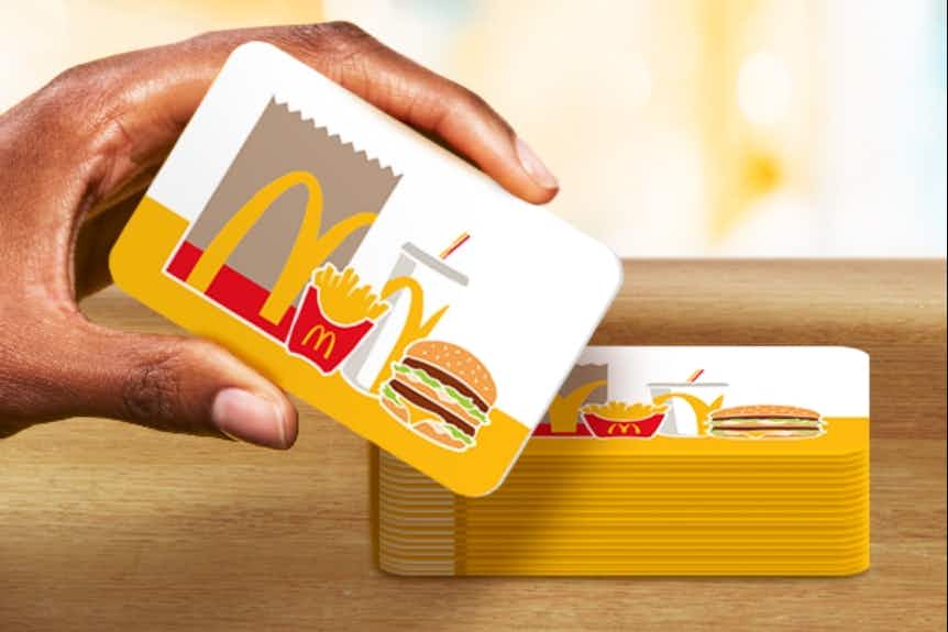 A person's hand holding a McDonald's Arch Card Gift Card next to a stack of more of the same gift card.